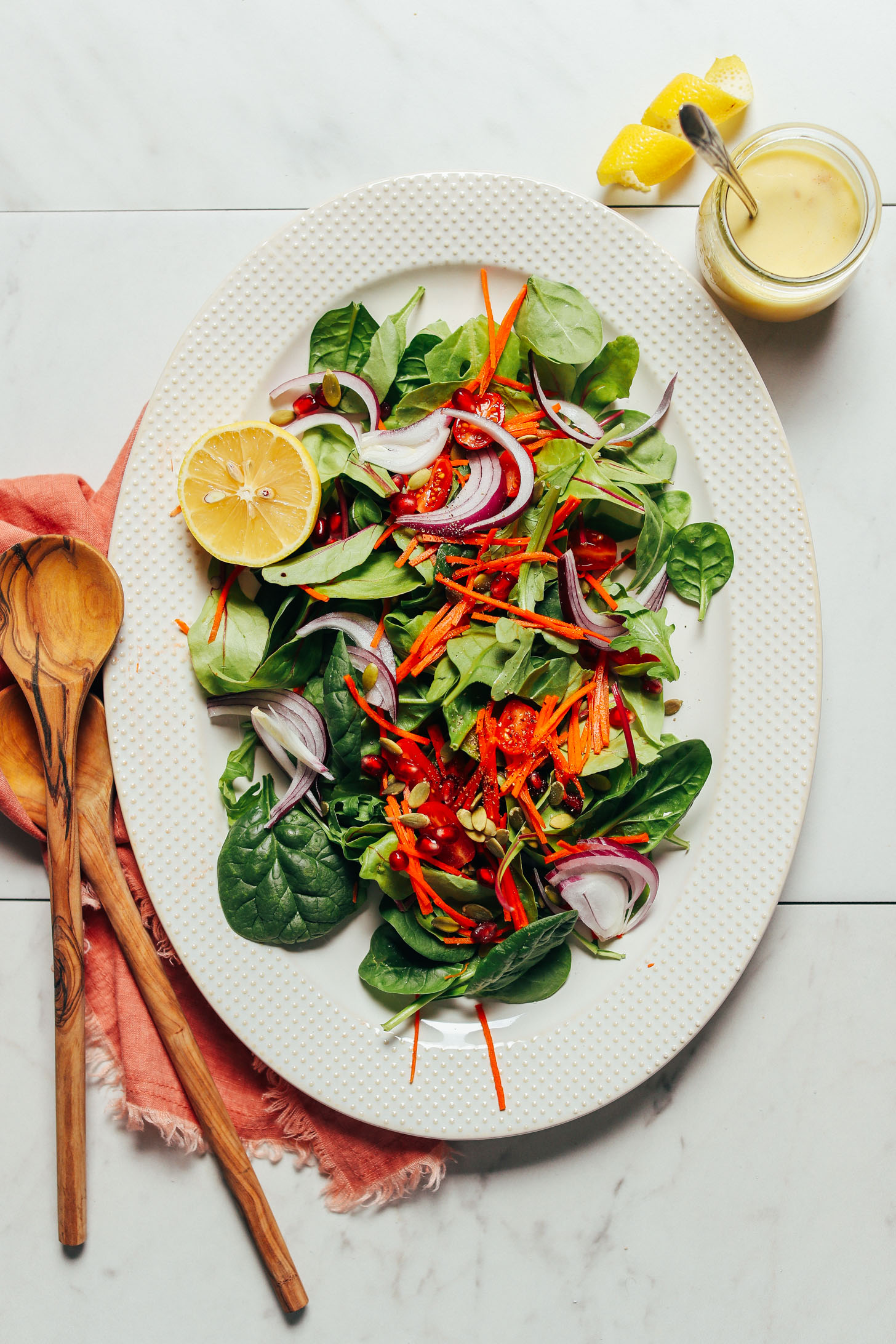 Overhead image of green salad with onion tomato carrots and lemon vinaigrette and tongs on the side