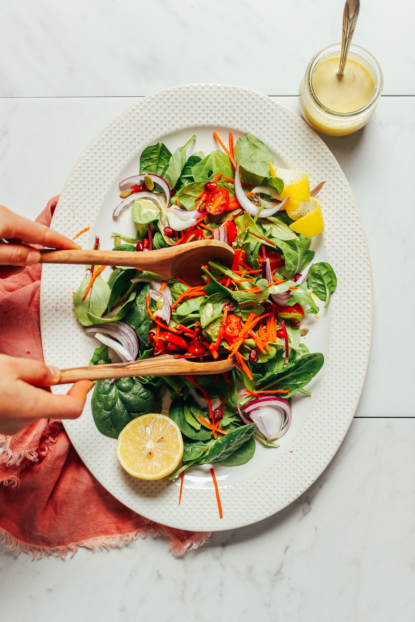 Overhead image of green salad with carrots tomato onion and lemon dressing and tongs tossing the salad