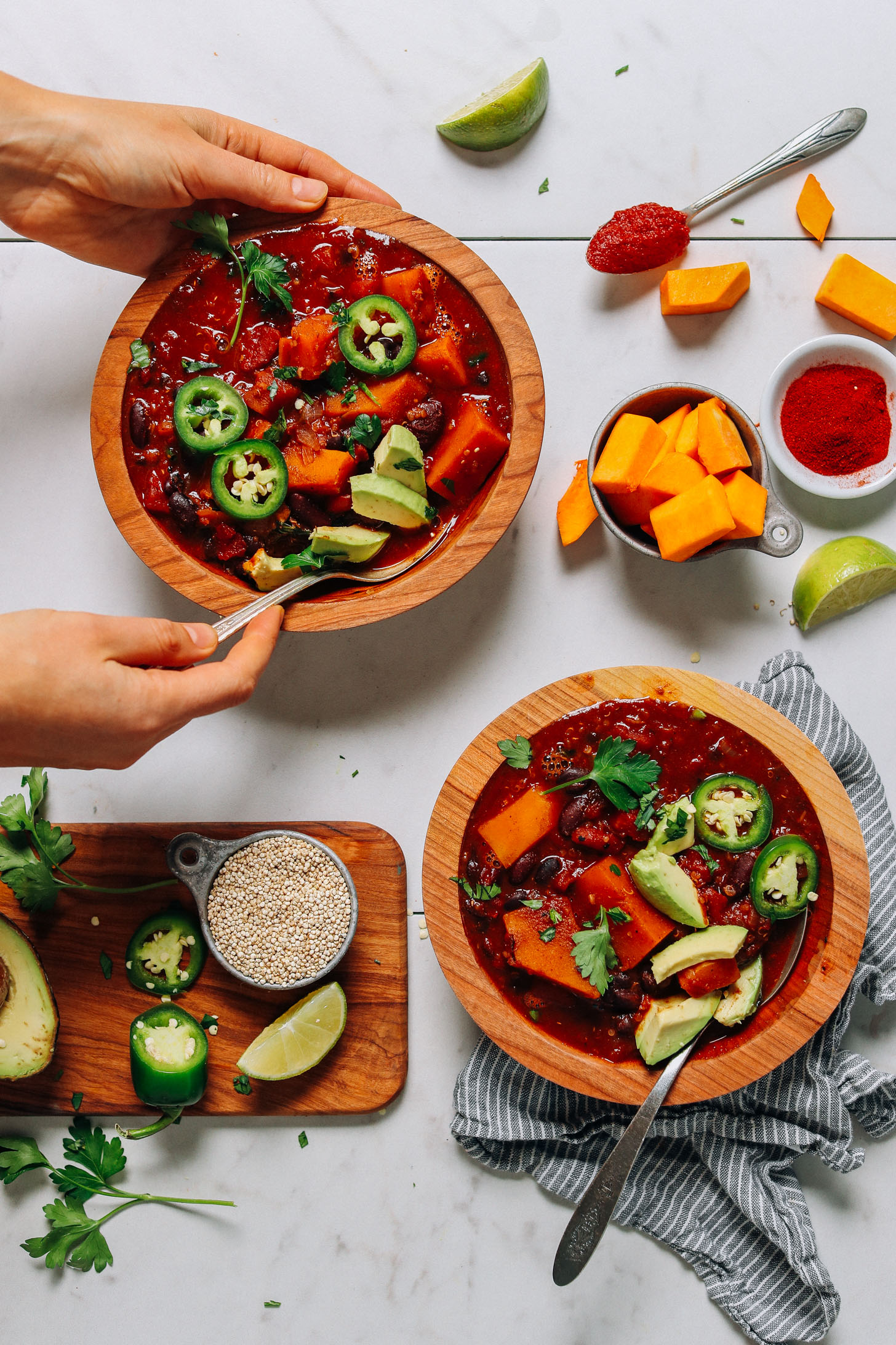 Bowls of Butternut Squash Quinoa Chili surrounded by ingredients used to make the recipe