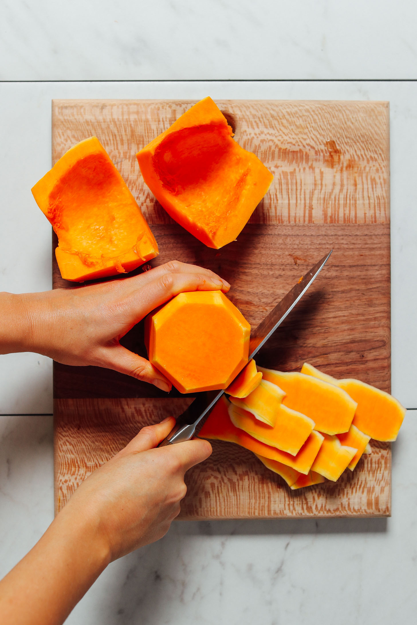 Using a large knife to cut the skin off of a butternut squash