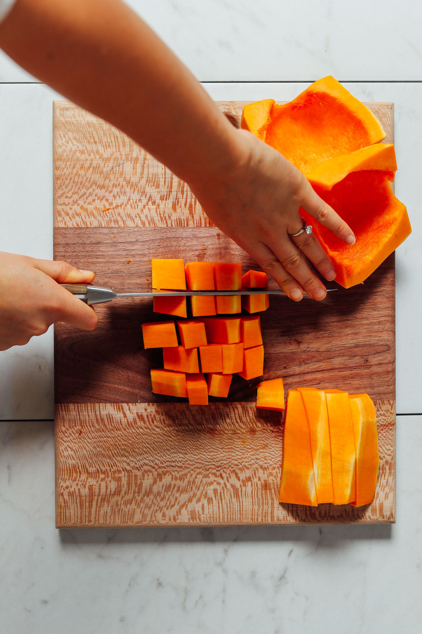 Cutting strips of butternut squash into cubes on a wood cutting board