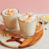 Two glass mugs filled with our Vegan White Hot Chocolate recipe alongside cinnamon sticks and cacao butter