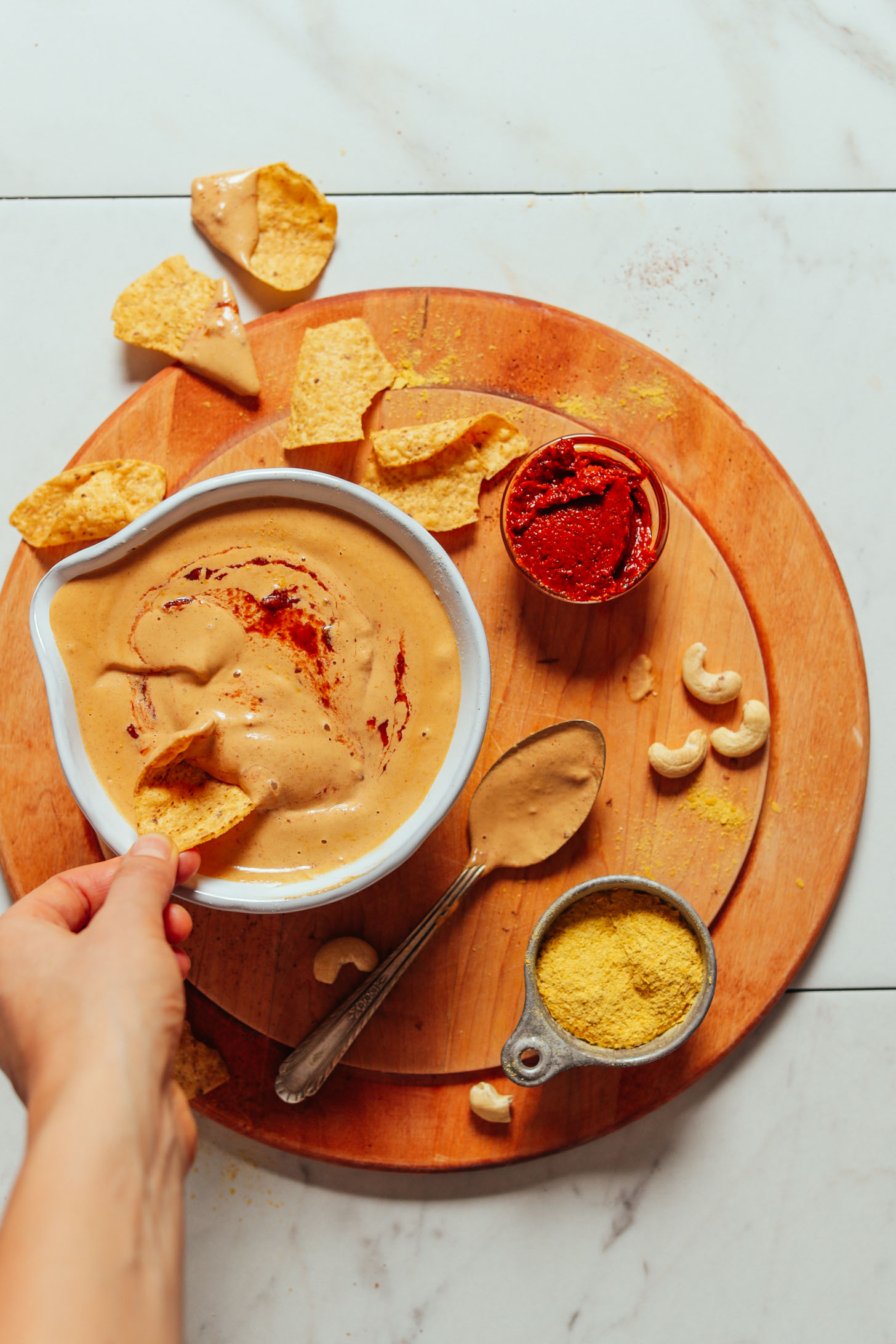 Overhead image of vegan cashew queso in a bowl with a hand dipping a dip