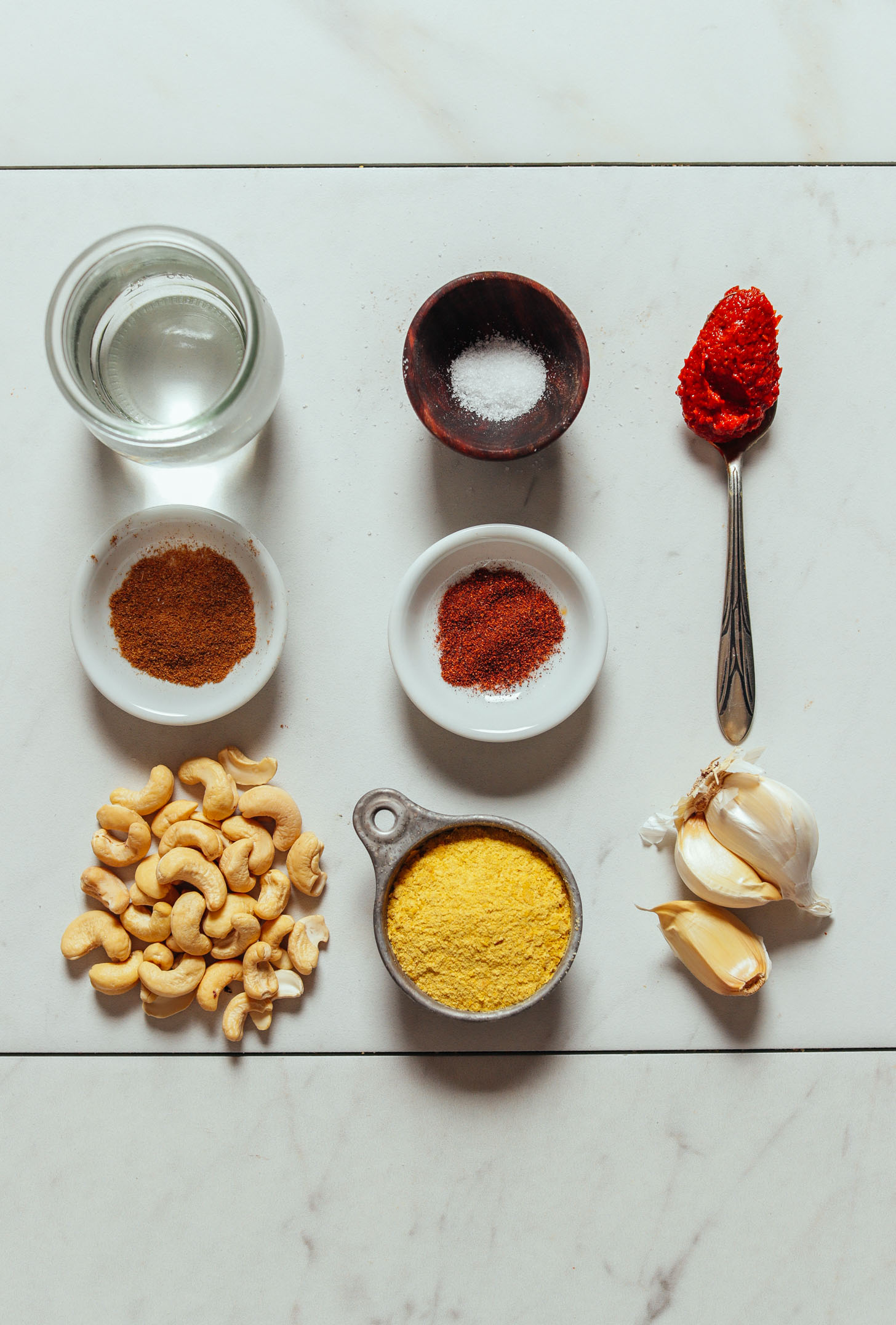 Overhead image of vegan cashew queso ingredients in a grid, including cashews, harissa, water, salt, and garlic