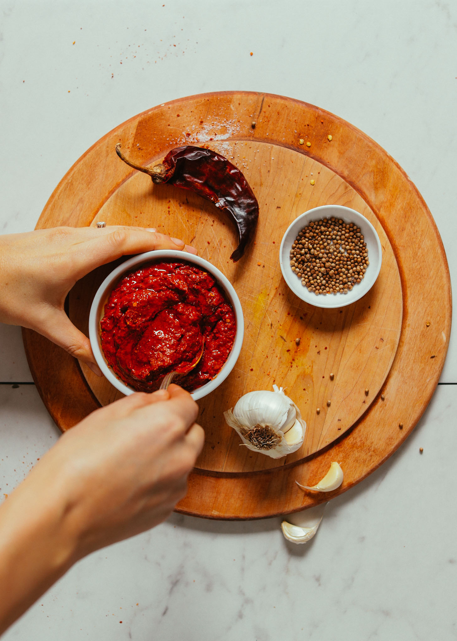 Stirring a bowl of Harissa Paste on a cutting board next to ingredients used to make it
