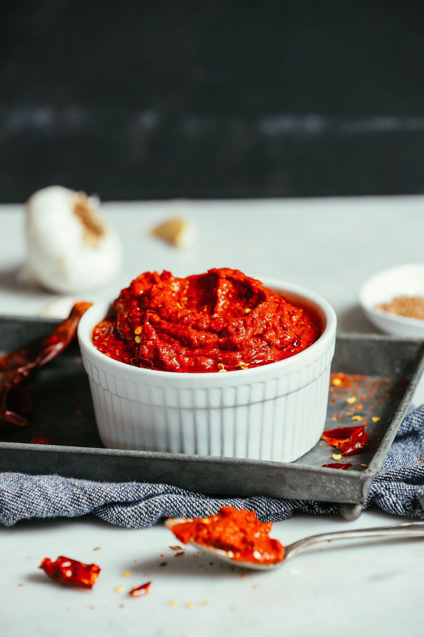 Bowl of our Harissa Paste recipe on a metal tray with garlic in the background
