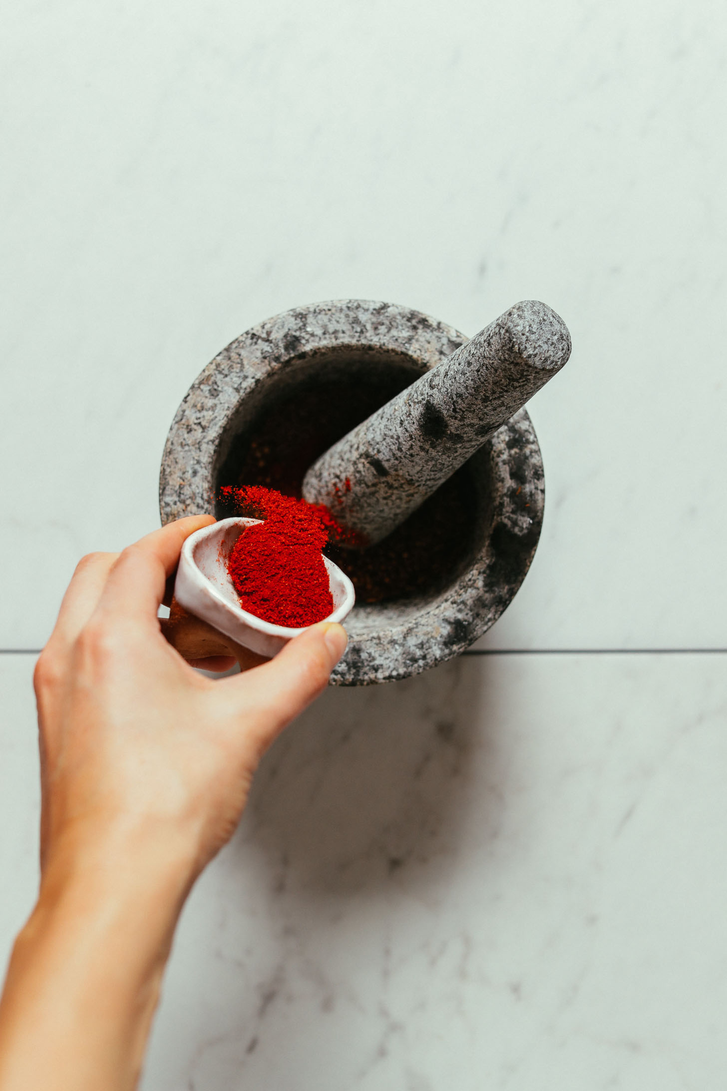 Overhead image of smoked paprika being shaken into a grey mortar and pestle