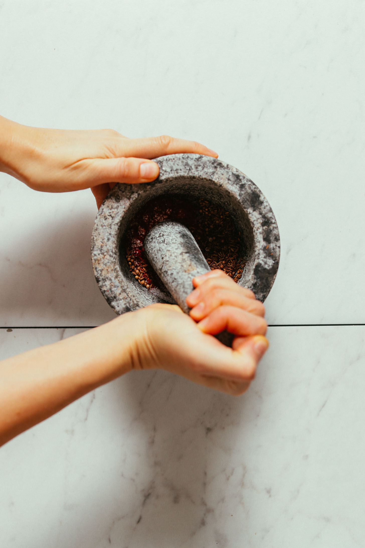 Whole spices being ground in a mortar and pestle for making Harissa Paste