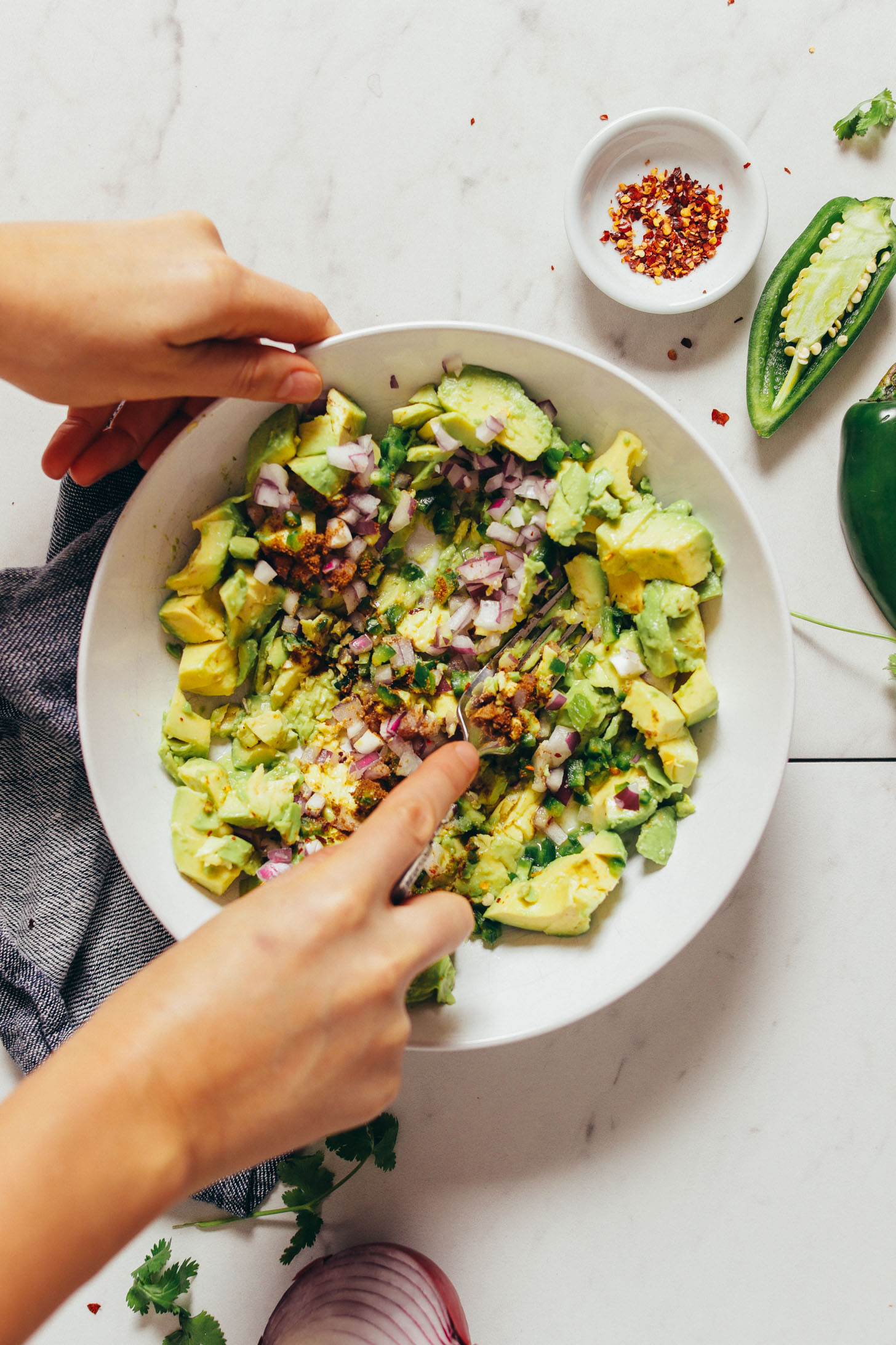 Overhead image of guacamole being mashed in a white bowl resting on a blue towel