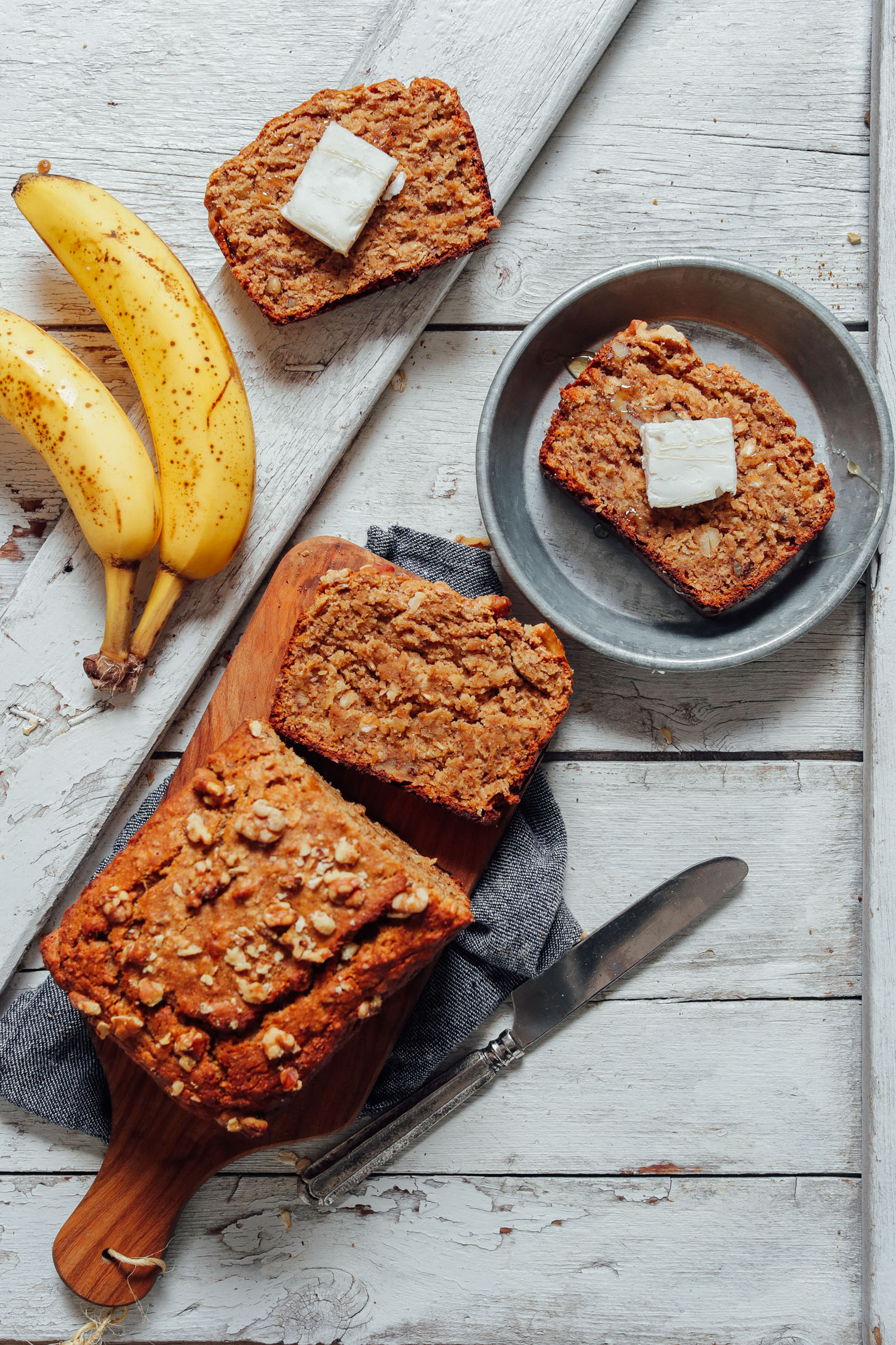 Overhead shot of vegan gluten free banana bread on cutting board with slices placed on metal plate and vegan butter on top