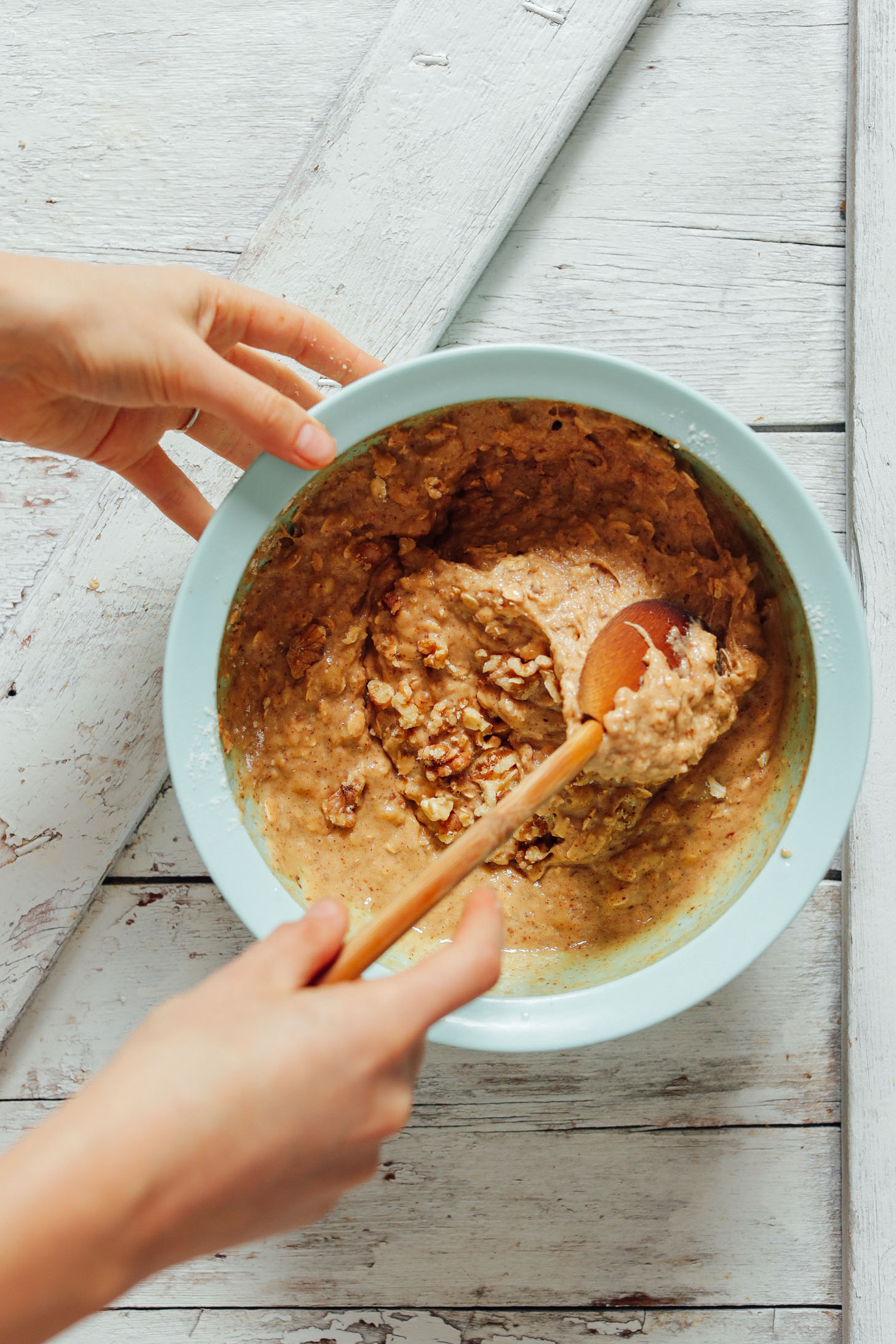 Overhead image of banana bread batter being mixed in a blue bowl with a wooden spoon