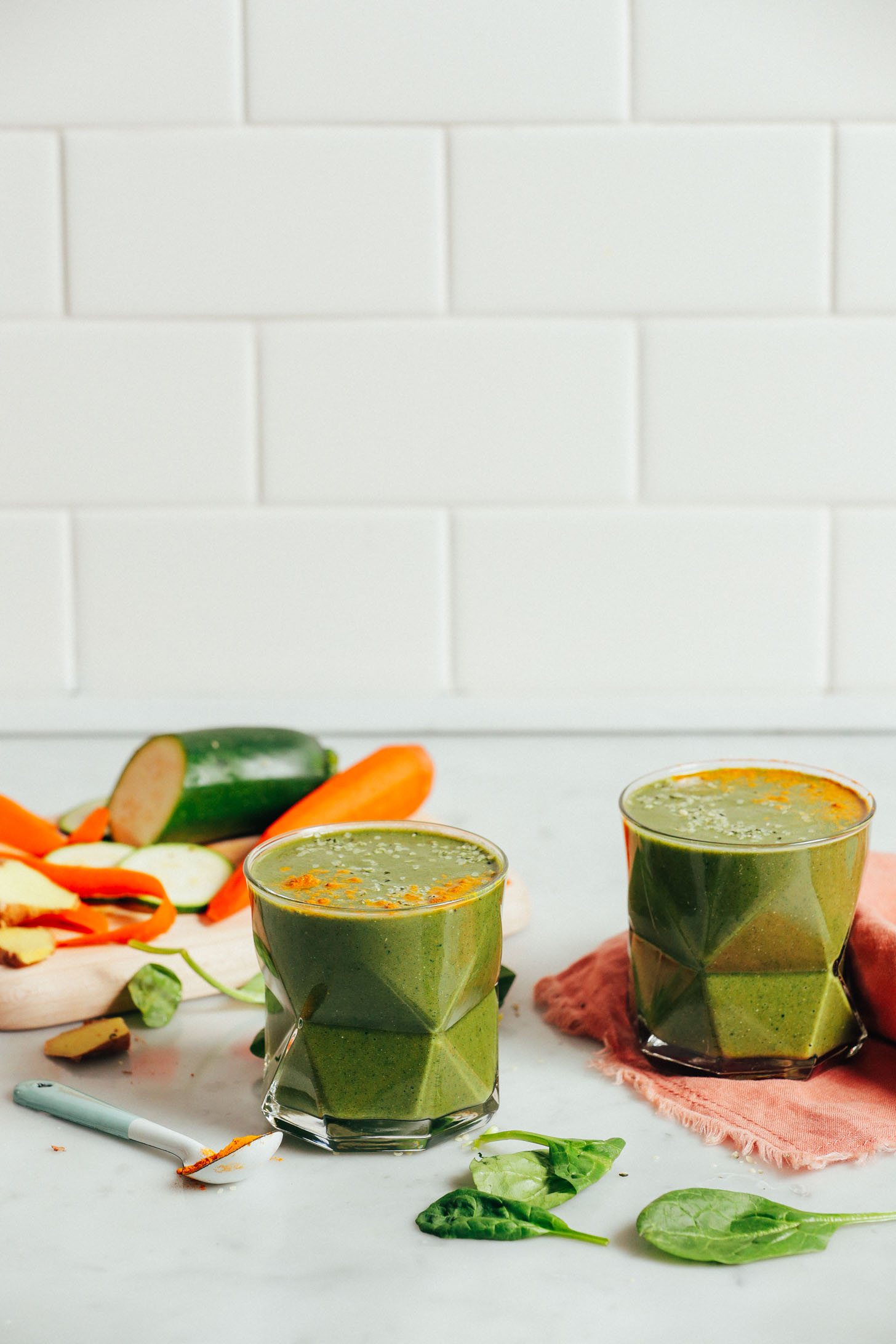 Straight on image of two glasses of warming winter green smoothie with carrot, zucchini, spinach, and turmeric garnish