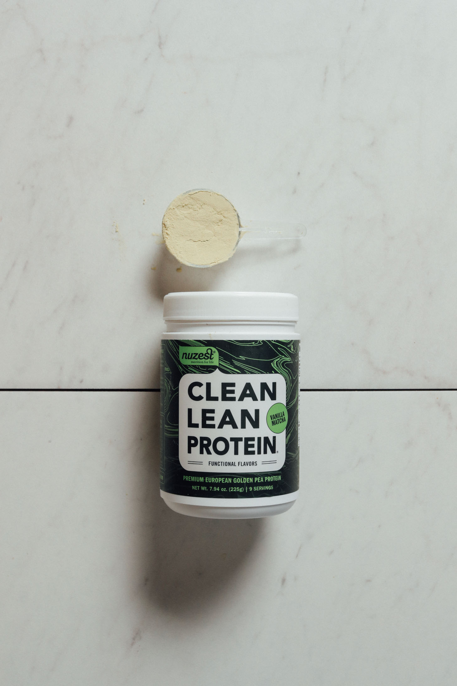 Tub and scoop of Nuzest Vanilla Matcha protein powder for our review