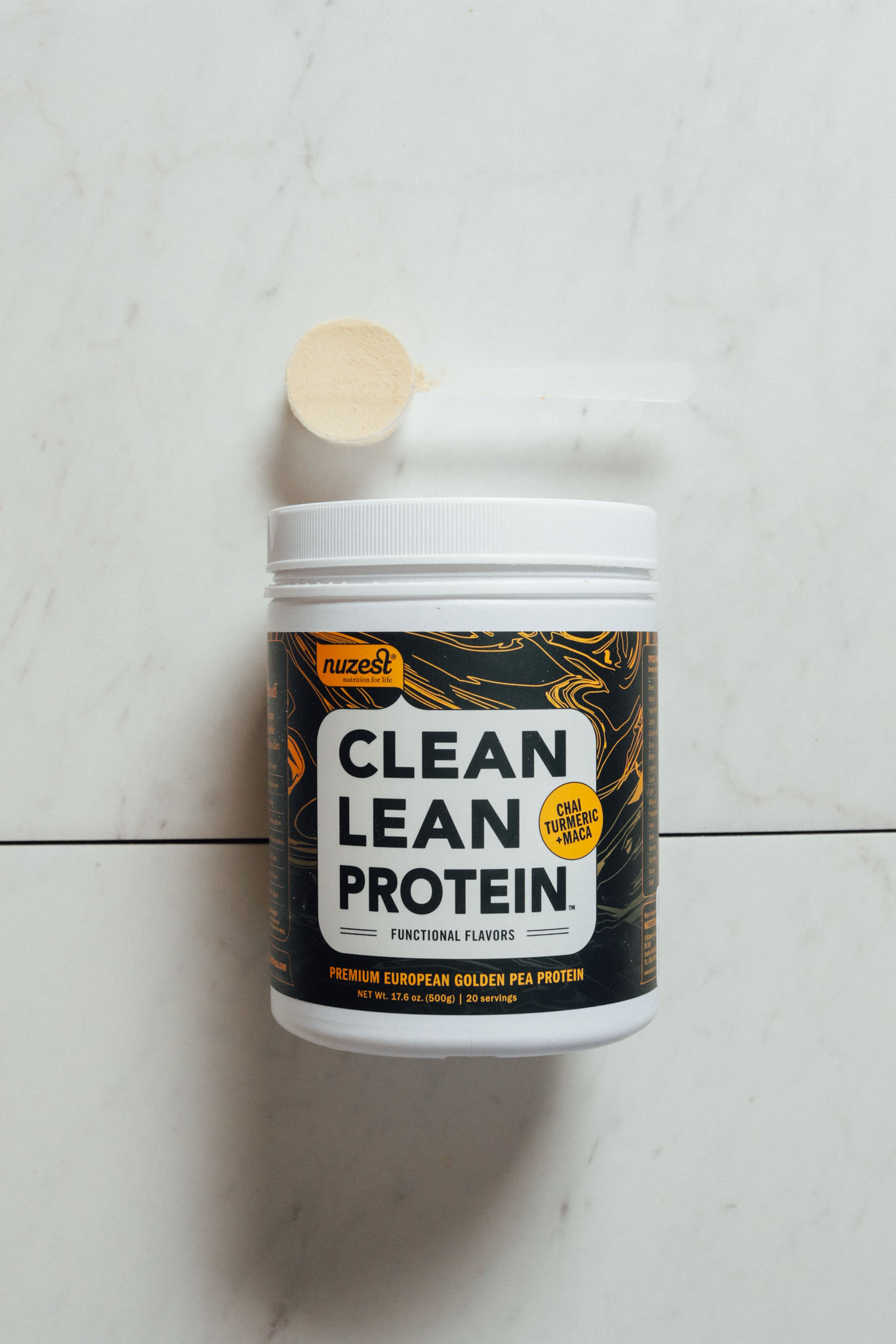 Tub and scoop of Nuzest Clean Lean Chai Turmeric Maca protein powder
