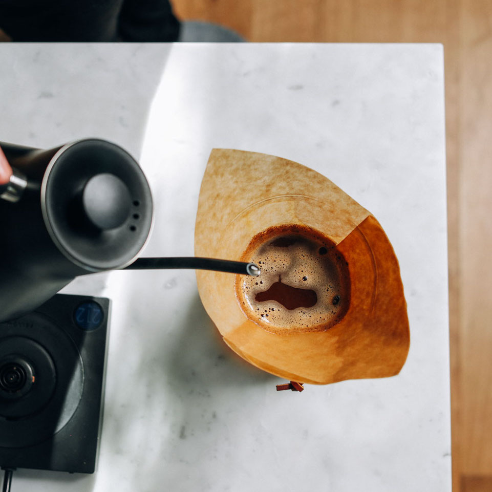 Pouring hot water from a kettle into a drip coffee maker