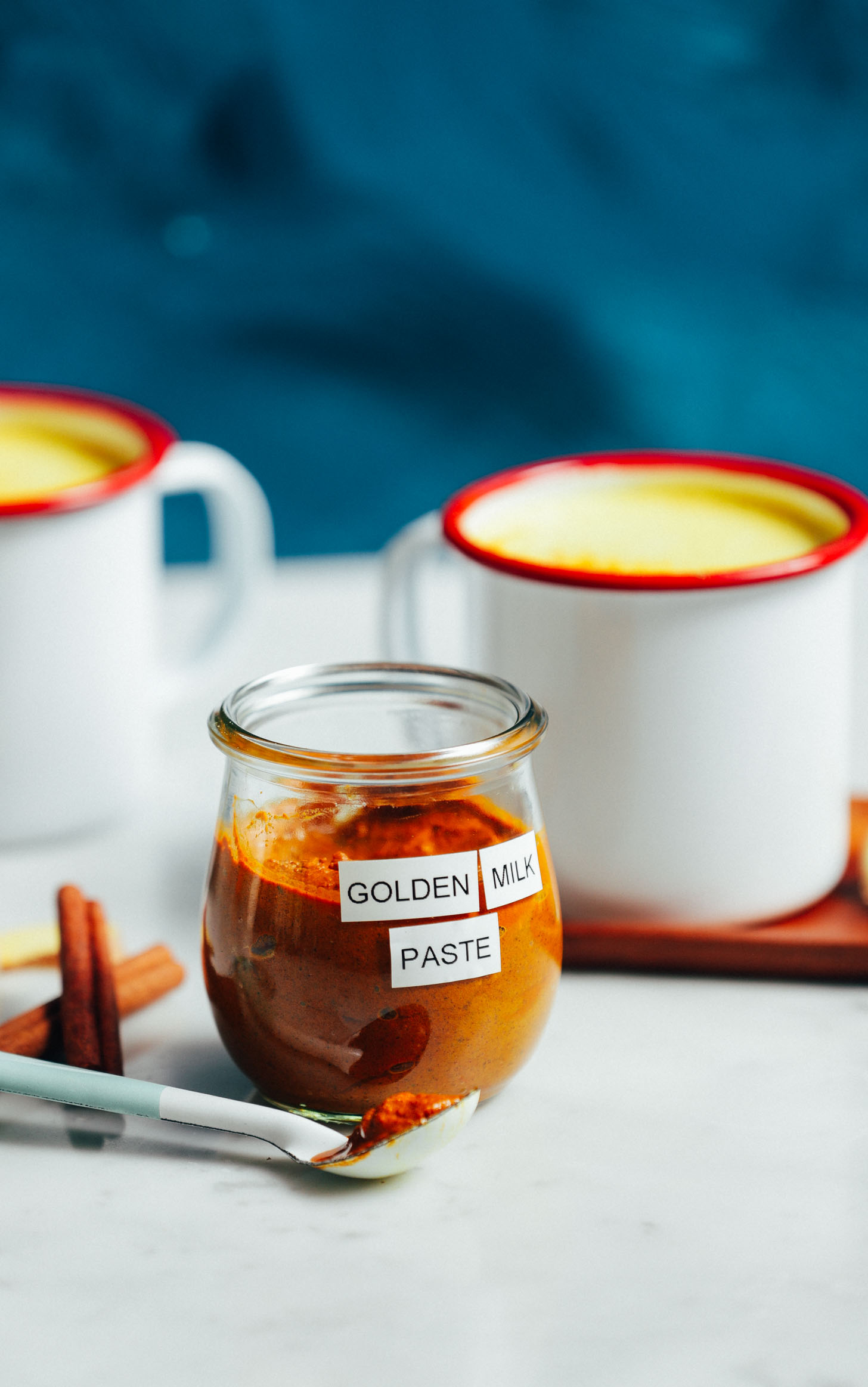 Jar of golden milk mix with two mugs of golden milk behind it