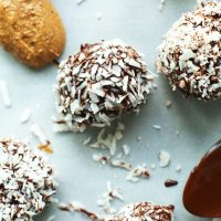 Spoonfuls of almond butter and dark chocolate beside Vegan Chocolate Snowballs made with dates