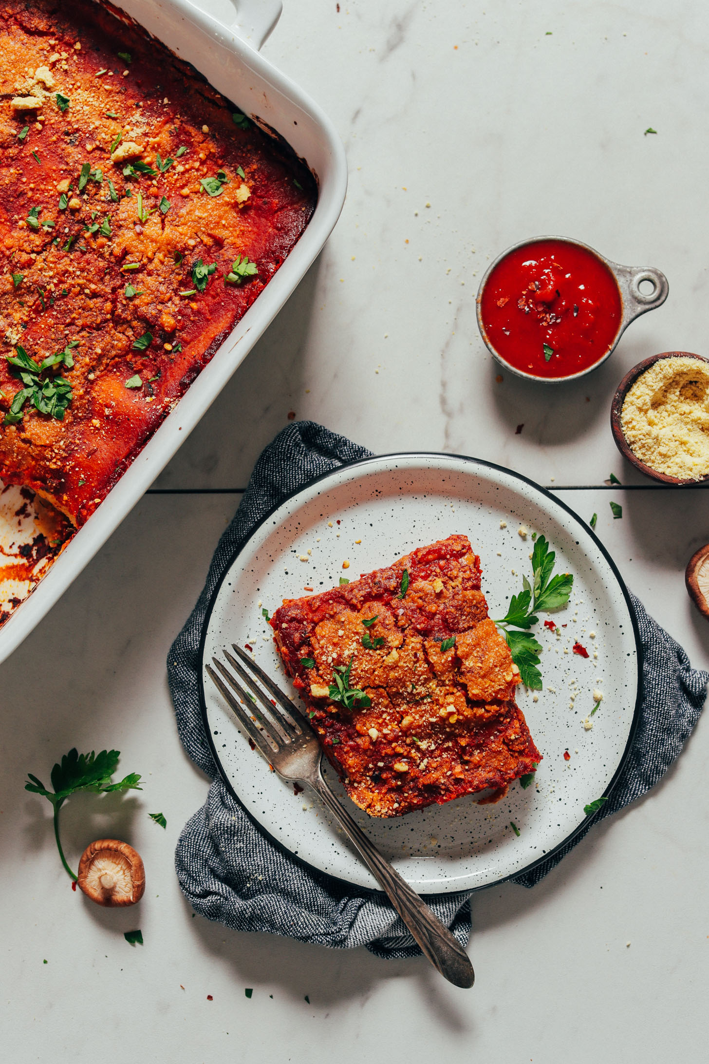 Slice of Vegan Lasagna alongside marinara, Vegan Parmesan, and the rest of the batch of lasagna