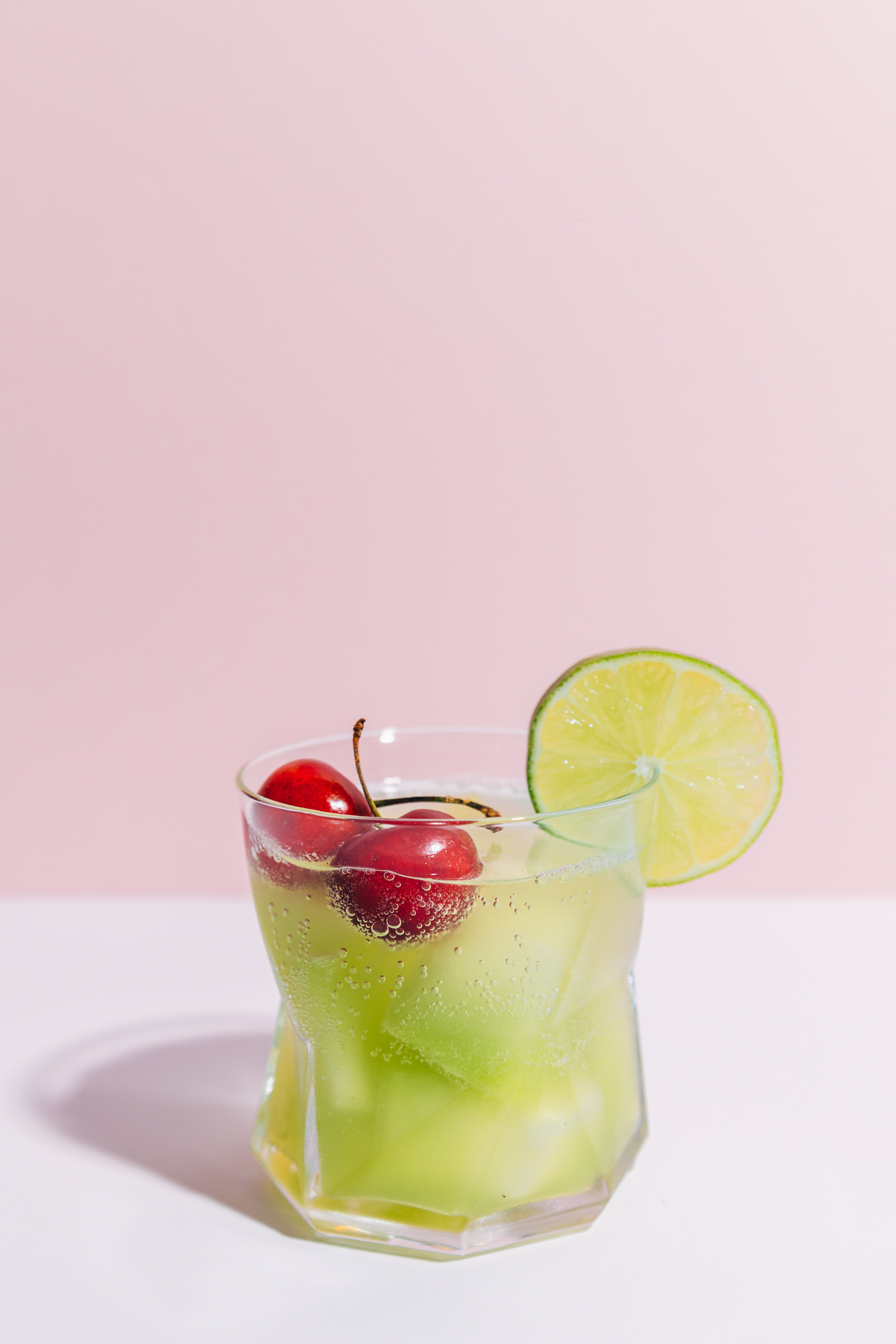 Glass of our Citrus and Melon Spritzer recipe garnished with fresh cherries and a lime slice