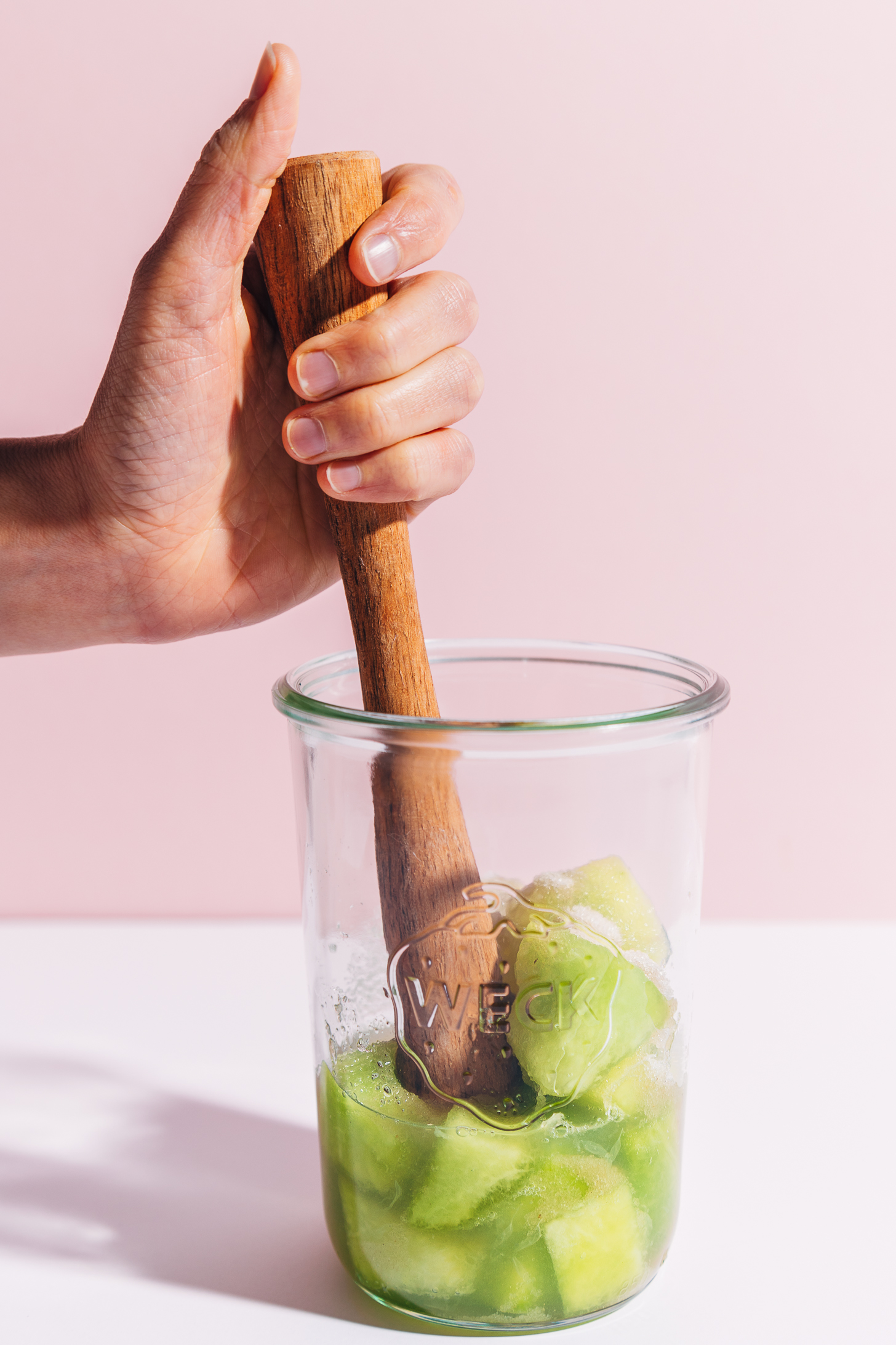Using a muddler to mix fresh honeydew melon with other ingredients for our Citrus and Melon Spritzer recipe
