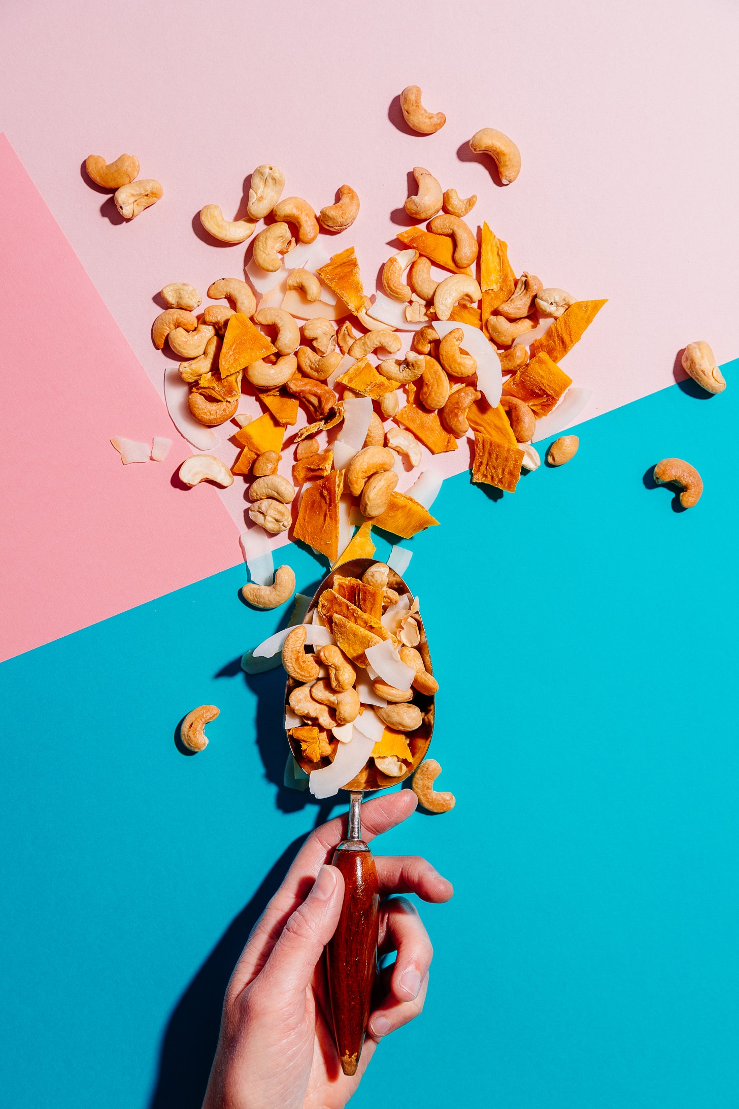 Using a spoon to pour homemade Tropical Trail Mix onto colorful paper
