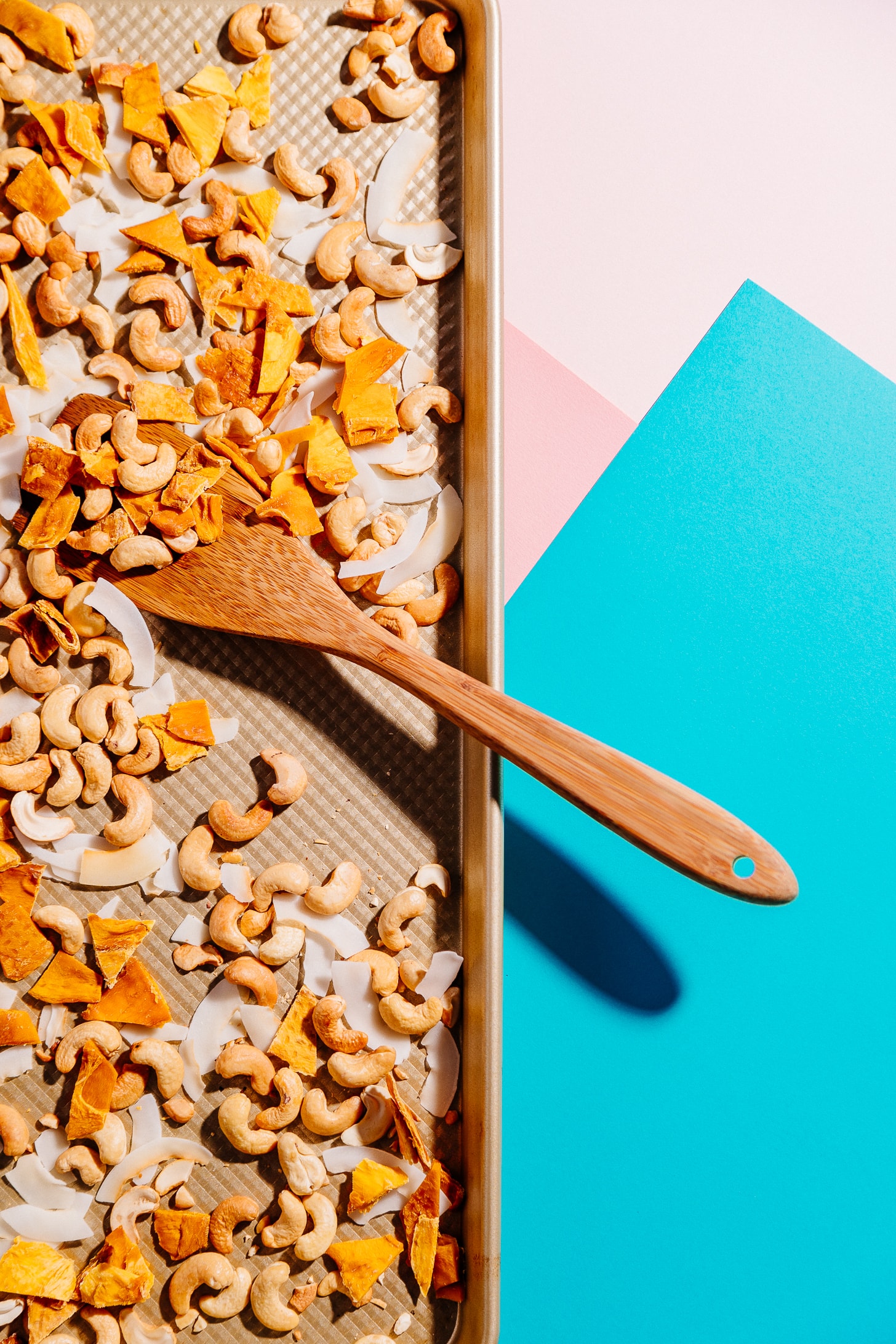Wooden spoon resting on a baking sheet of healthy homemade Tropical Trail Mix