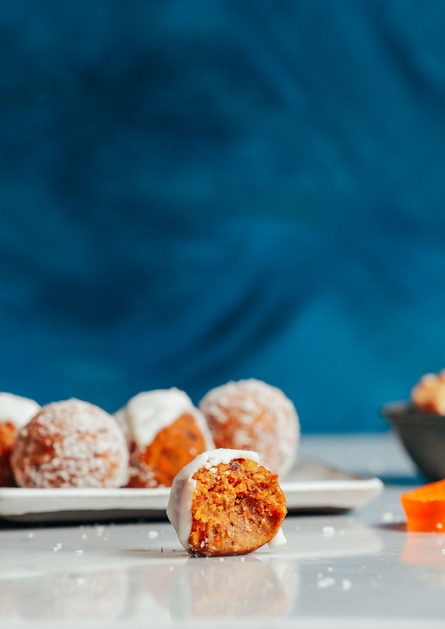 Half-eaten Raw Carrot Cake Bite resting in front of a tray of more bites