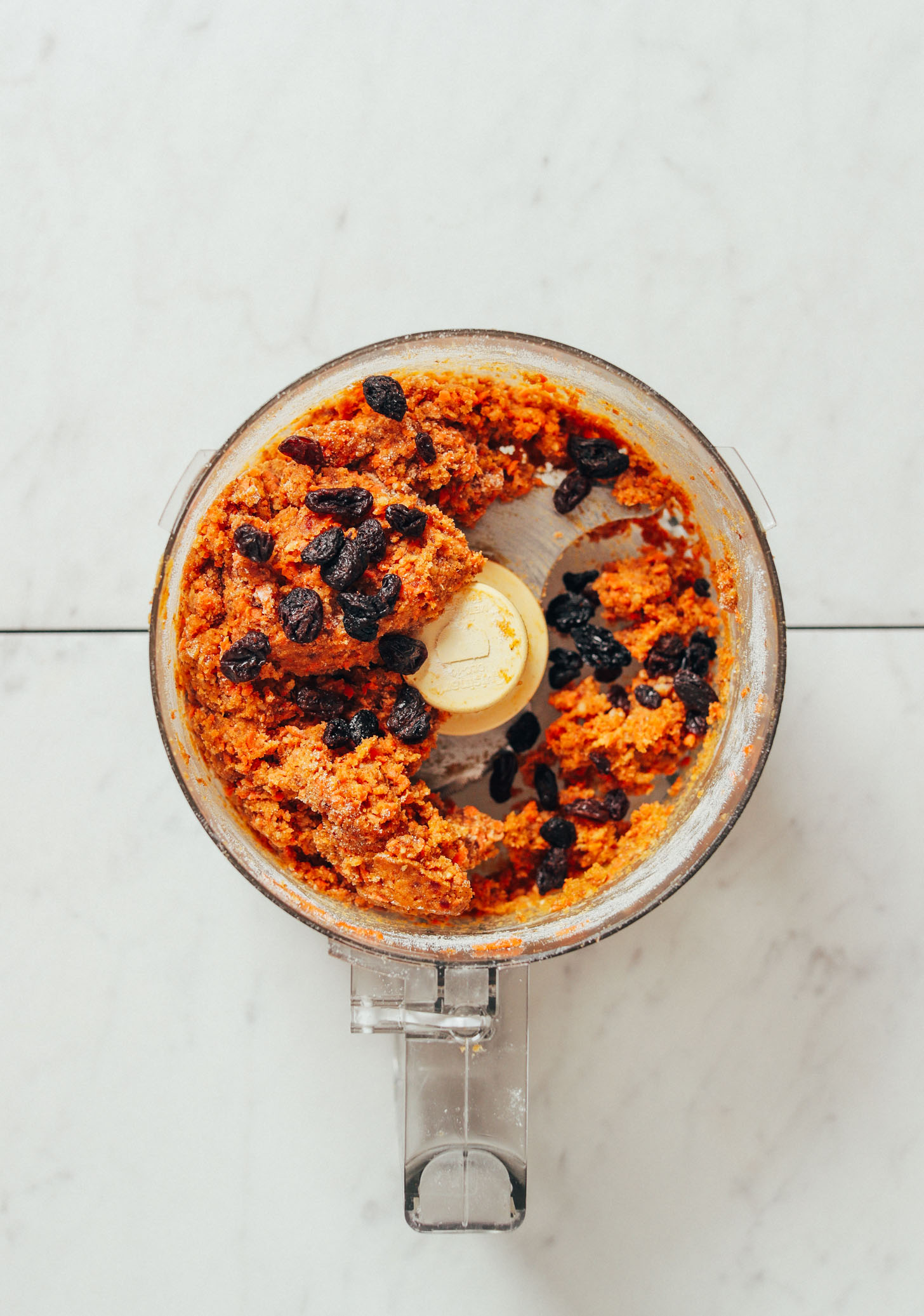 Food processor with Raw Carrot Cake Bite batter topped with raisins