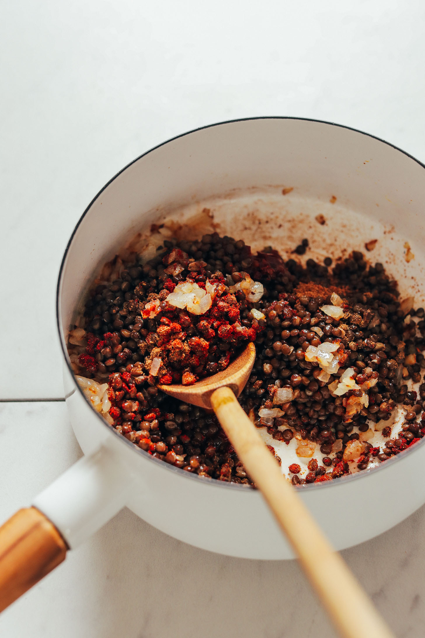 Using a wooden spoon to stir a pot of lentils and spices for making Smoky Refried Lentils