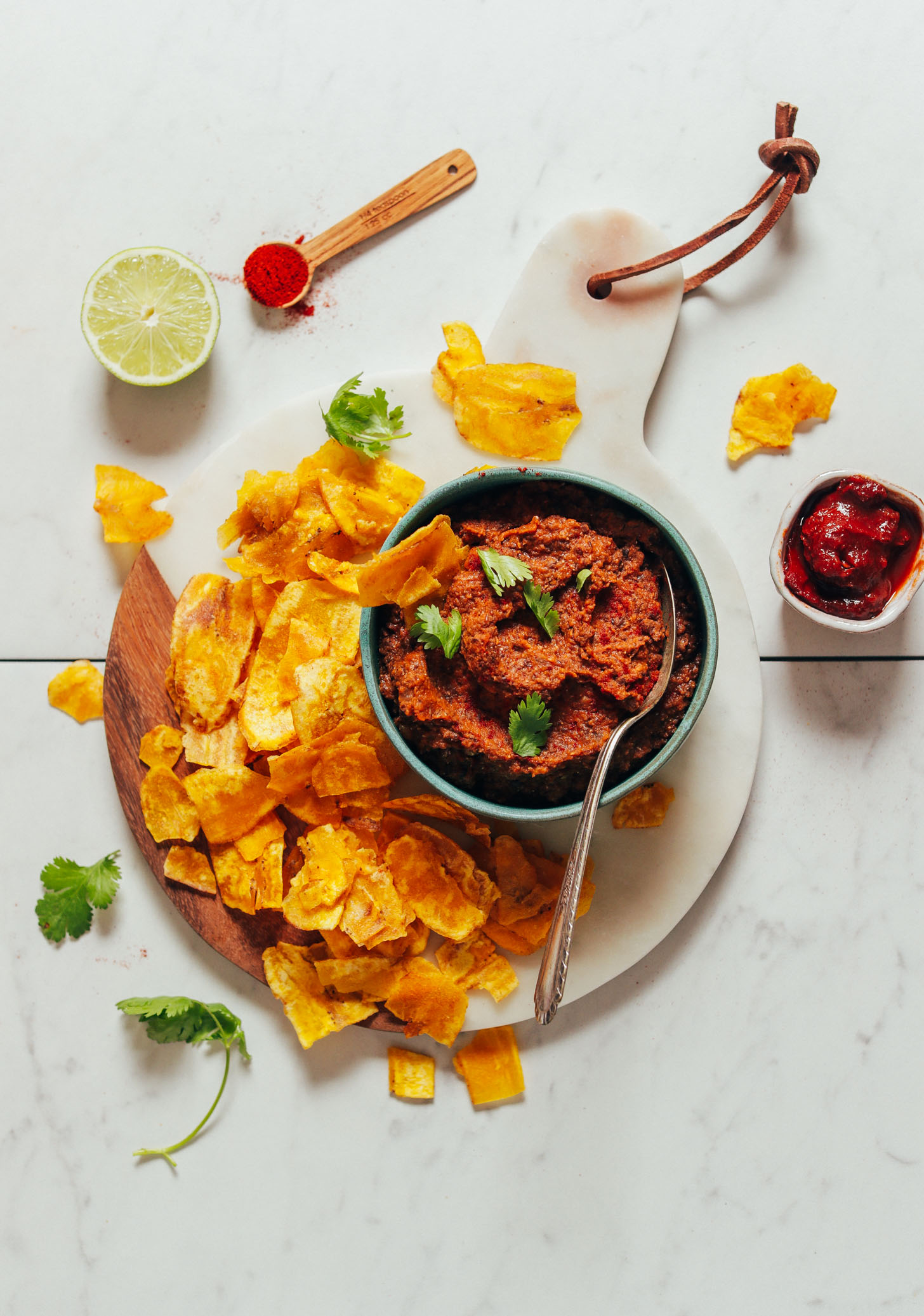 Wood and marble cutting board with a bowl of Smoky Refried Lentils and plantain chips