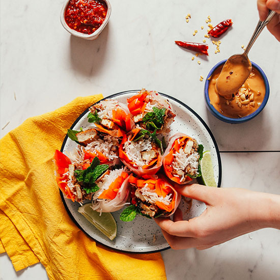 Adding peanut sauce to a Crispy Shallot Spring Roll for a delicious vegan appetizer