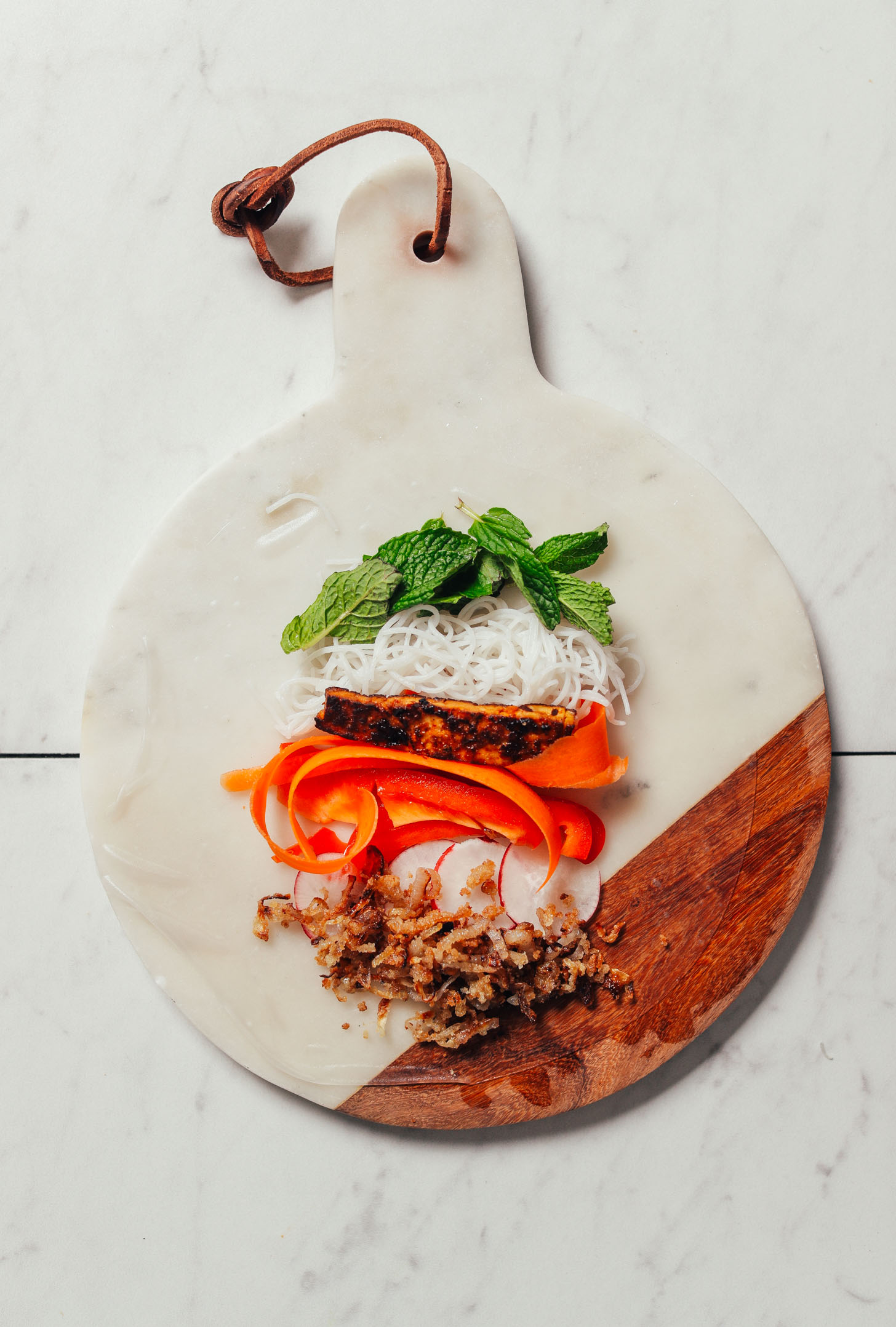 Marble and wood cutting board with a softened spring roll paper topped with fresh ingredients
