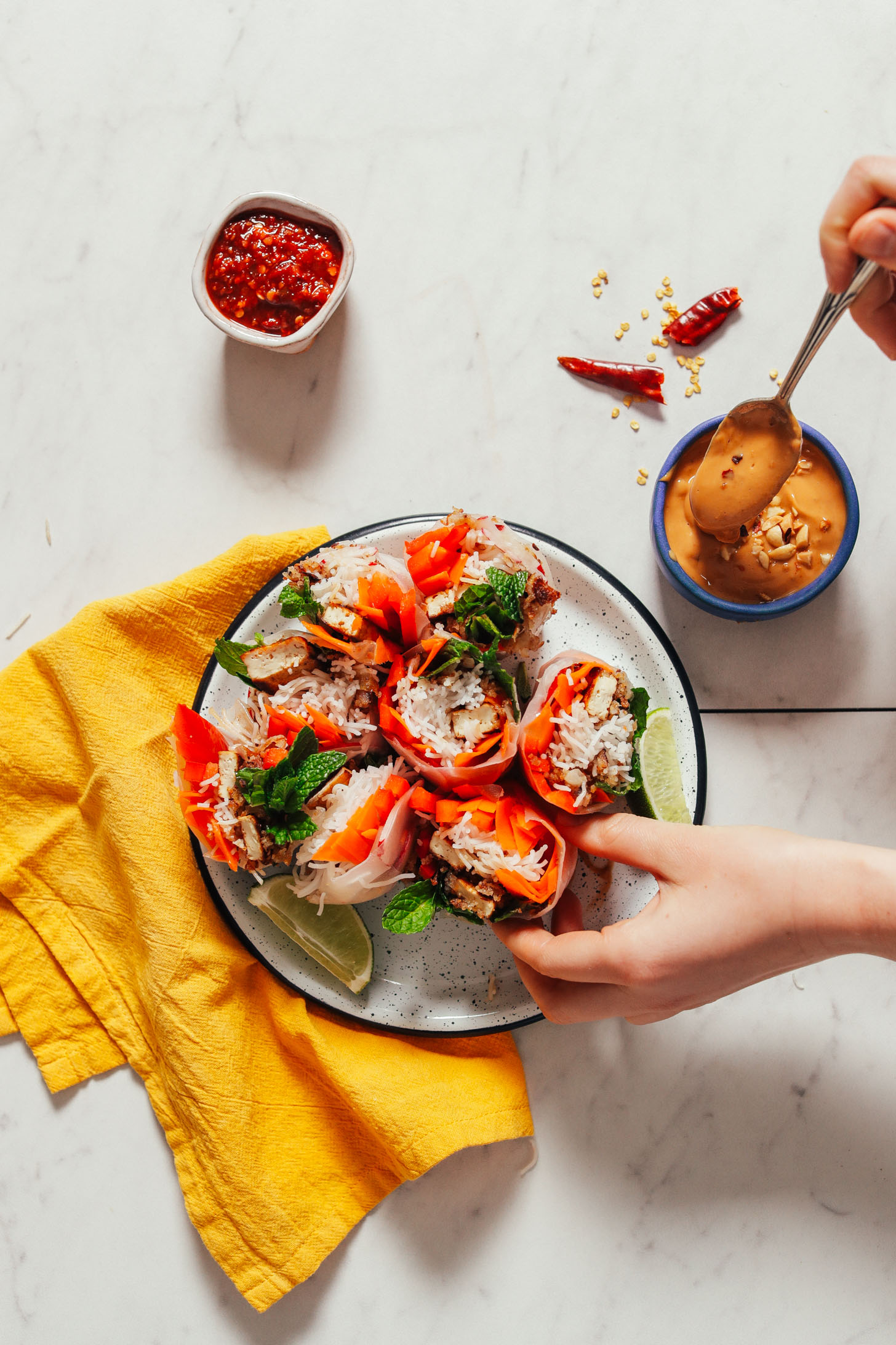 Using a spoon to ladle peanut sauce over a Crispy Shallot Spring Roll with Seared Tofu