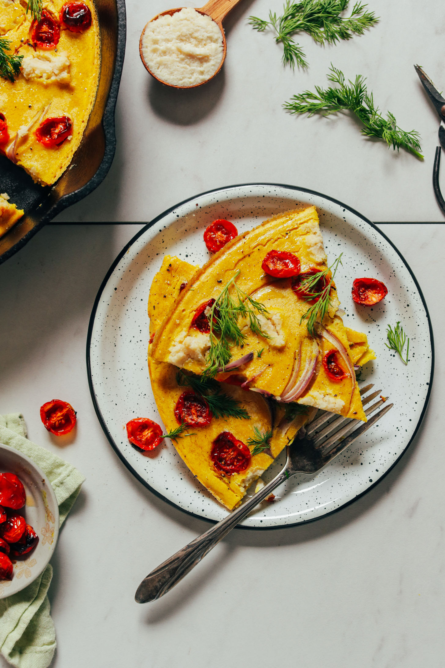 Plate with slices of Vegan Frittata topped with fresh dill and slow roasted tomatoes