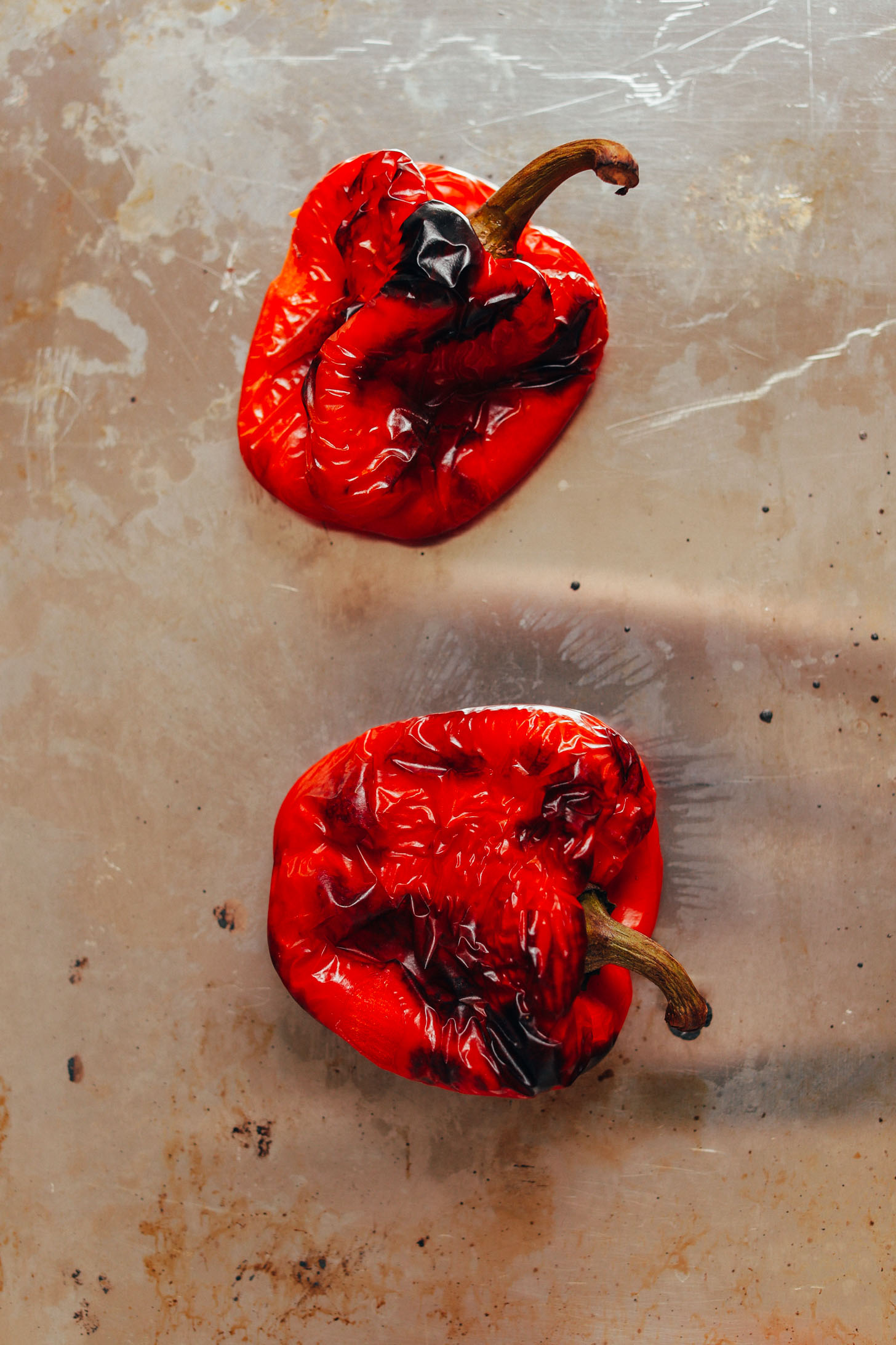 Baking sheet with two freshly roasted red bell peppers for making Romesco Sauce