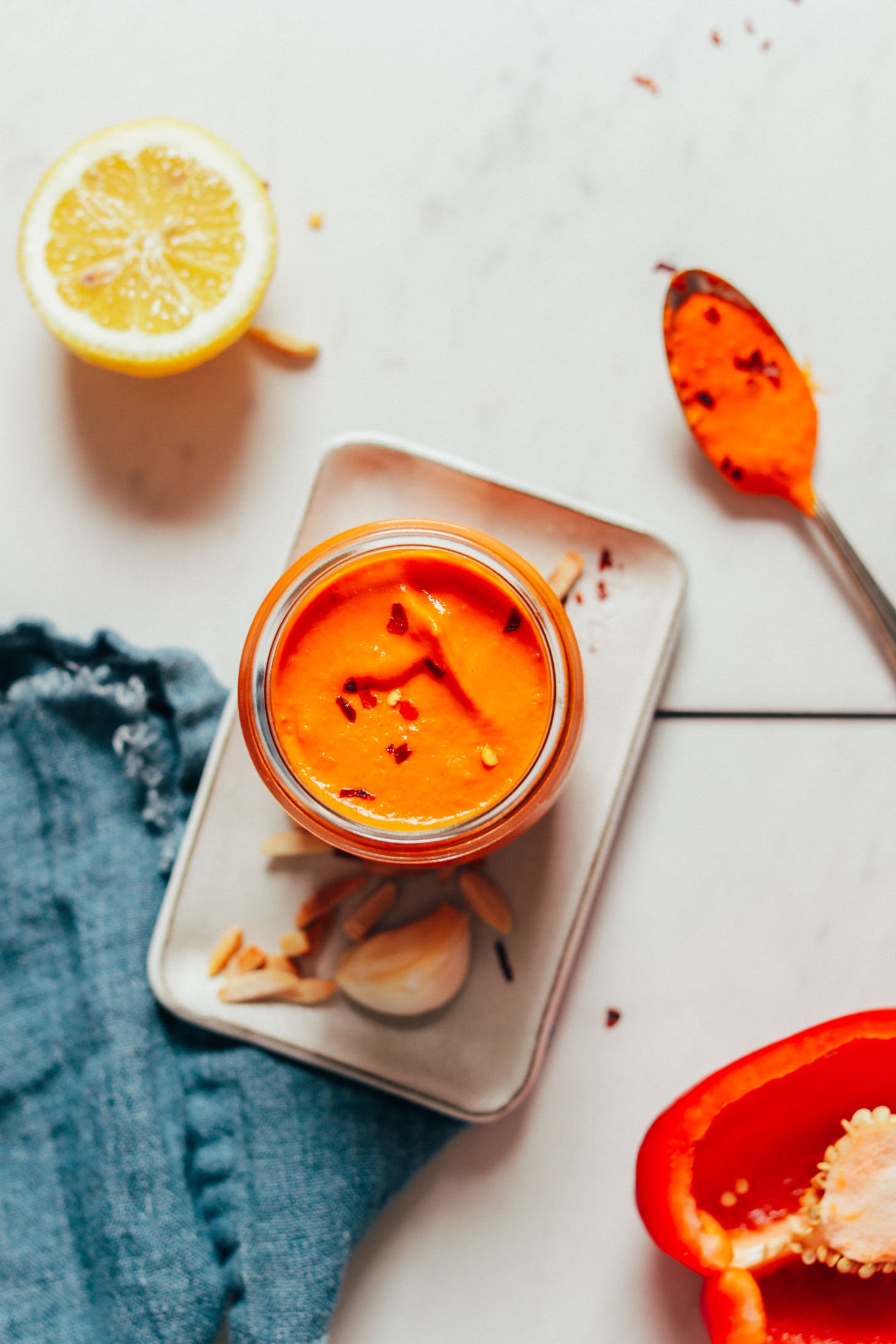 Top-down shot of a jar of our simple Romesco Sauce recipe beside ingredients used to make it