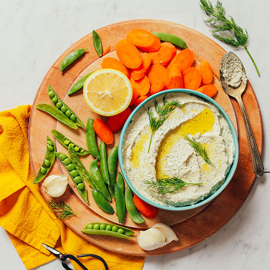 Bowl of Garlic Dill Sunflower Dip on a wood cutting board with fresh vegetables for dipping