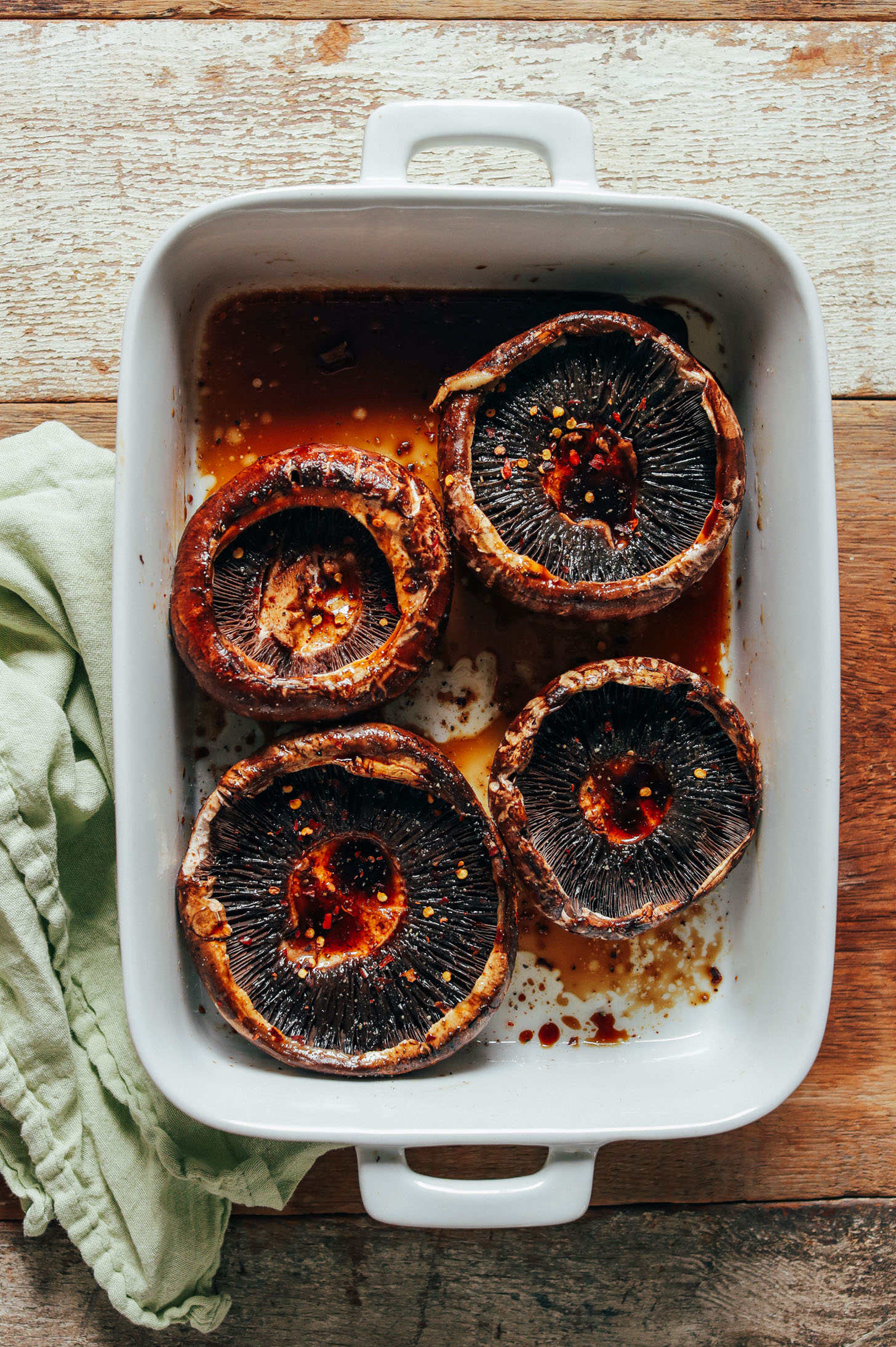 White ceramic baking dish filled with portobello mushrooms marinating in balsamic vinegar