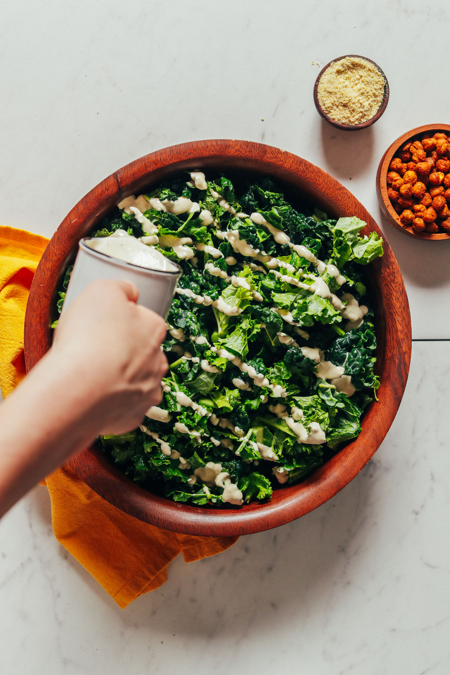 Drizzling chickpea caesar salad dressing onto chopped kale