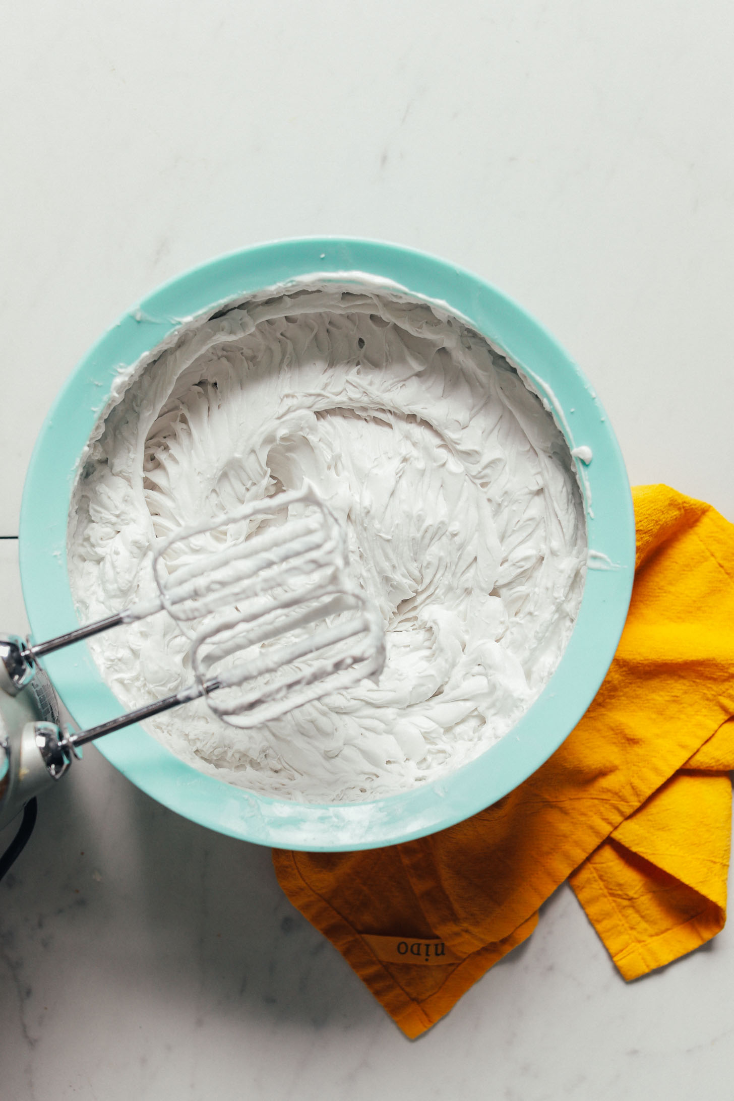 Egg beaters resting above a bowl of vegan whipped cream