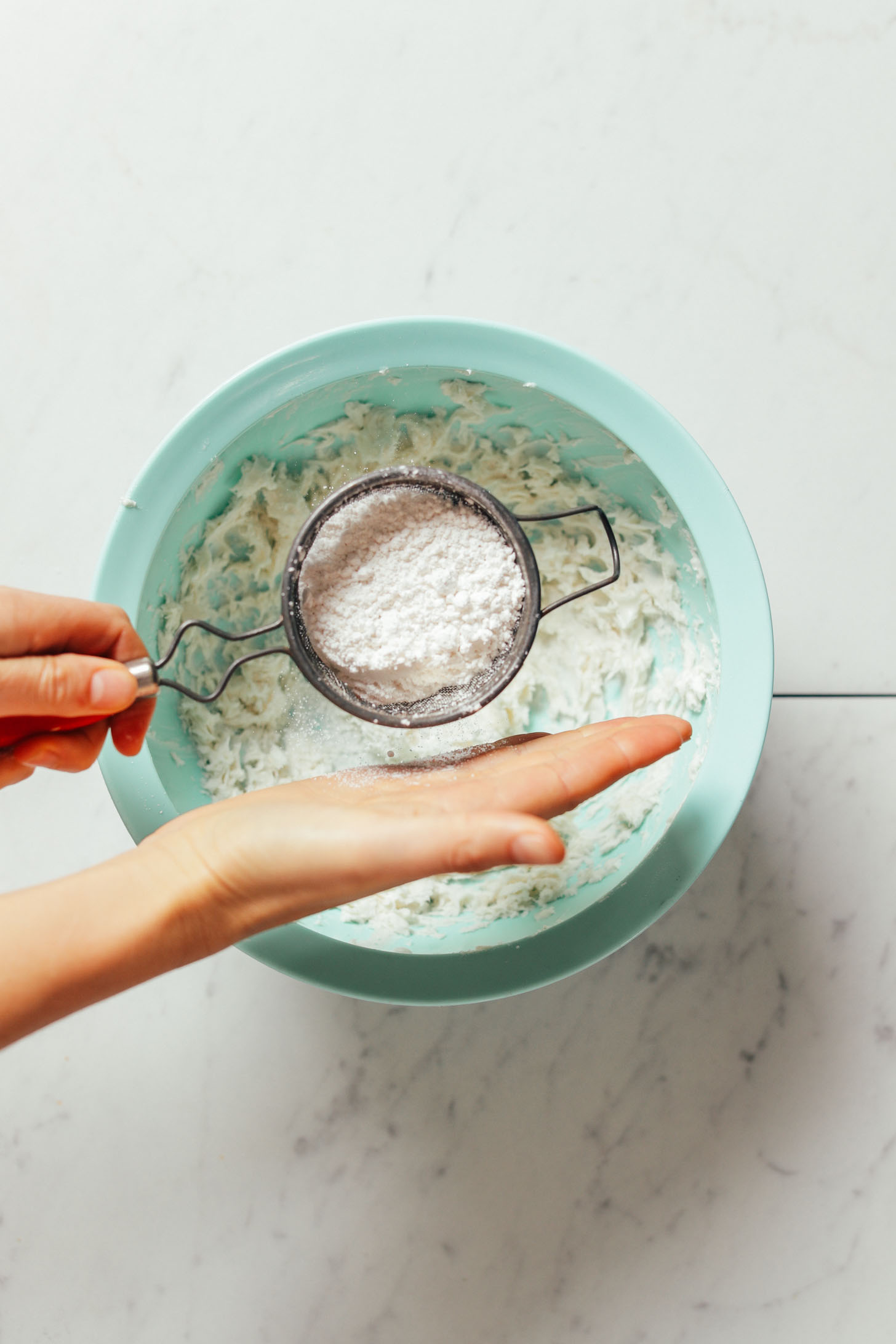 Sifting powdered sugar into vegan butter to make Vegan Buttercream Frosting