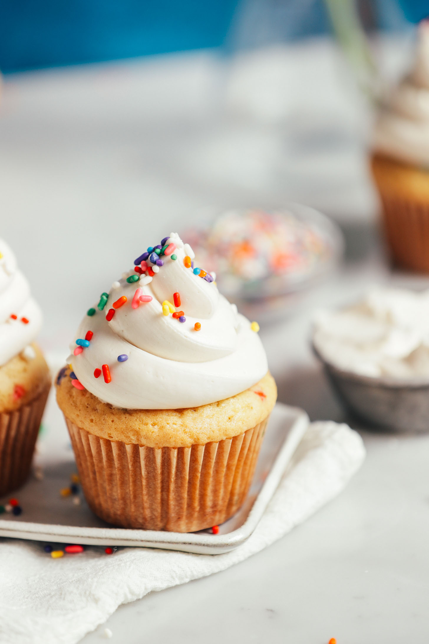 Close up shot of a plate of cupcakes topped with Vegan Buttercream Frosting and rainbow sprinkles