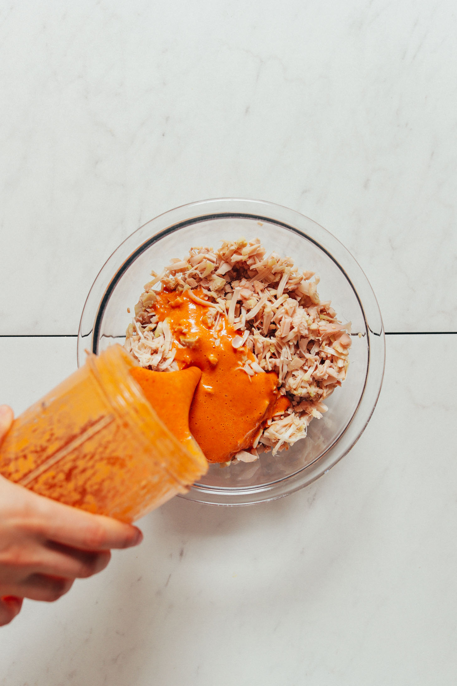 Pouring smoky sauce from a small blender into a bowl of shredded jackfruit
