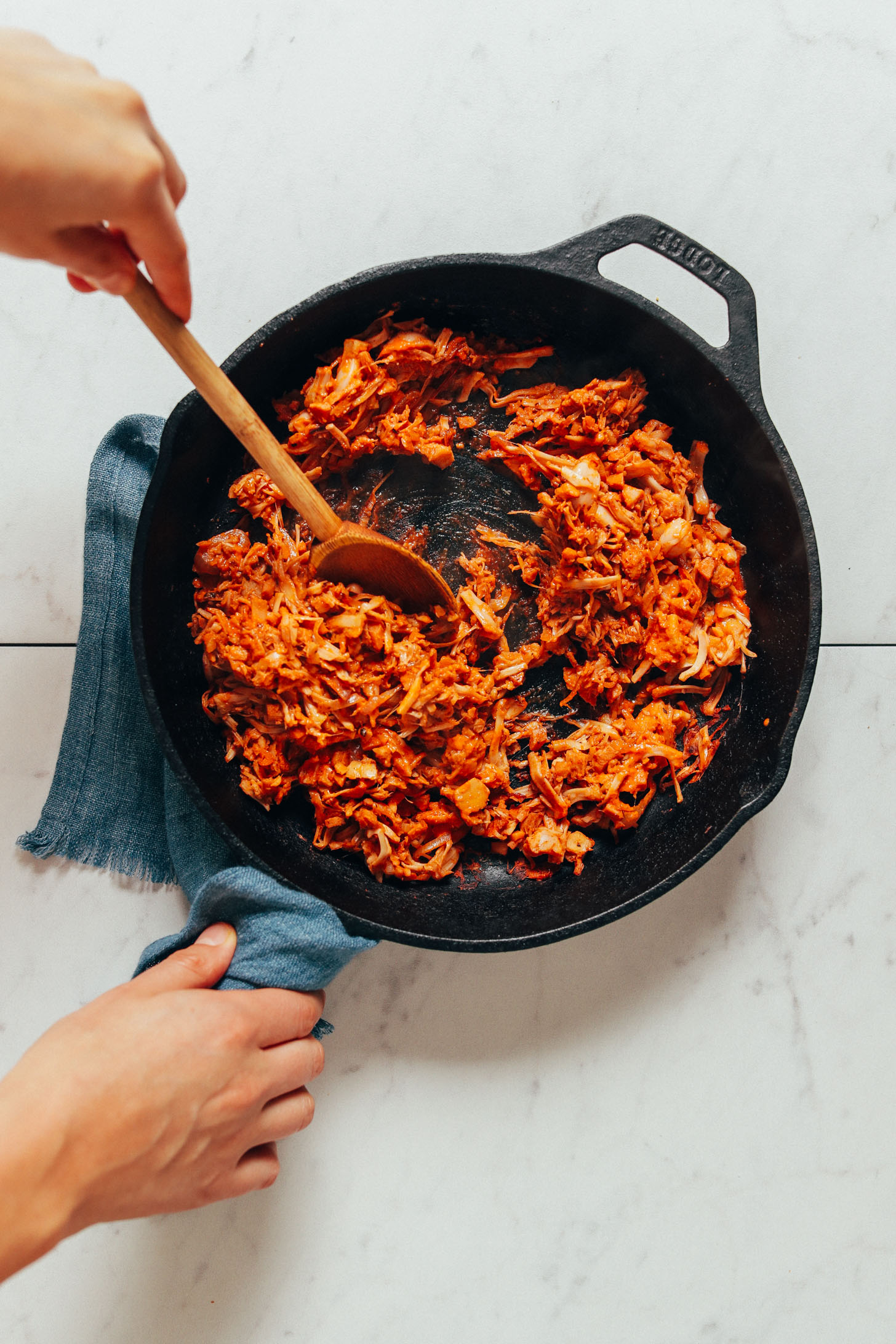Using a wooden spoon to stir a skillet of Smoky Marinated Jackfruit
