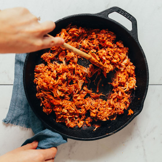 Using a wooden spoon to stir a pan of our Smoky Jackfruit recipe