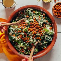 Using salad tongs to pick up a serving of our delicious Kale Caesar Salad with Crispy Chickpeas
