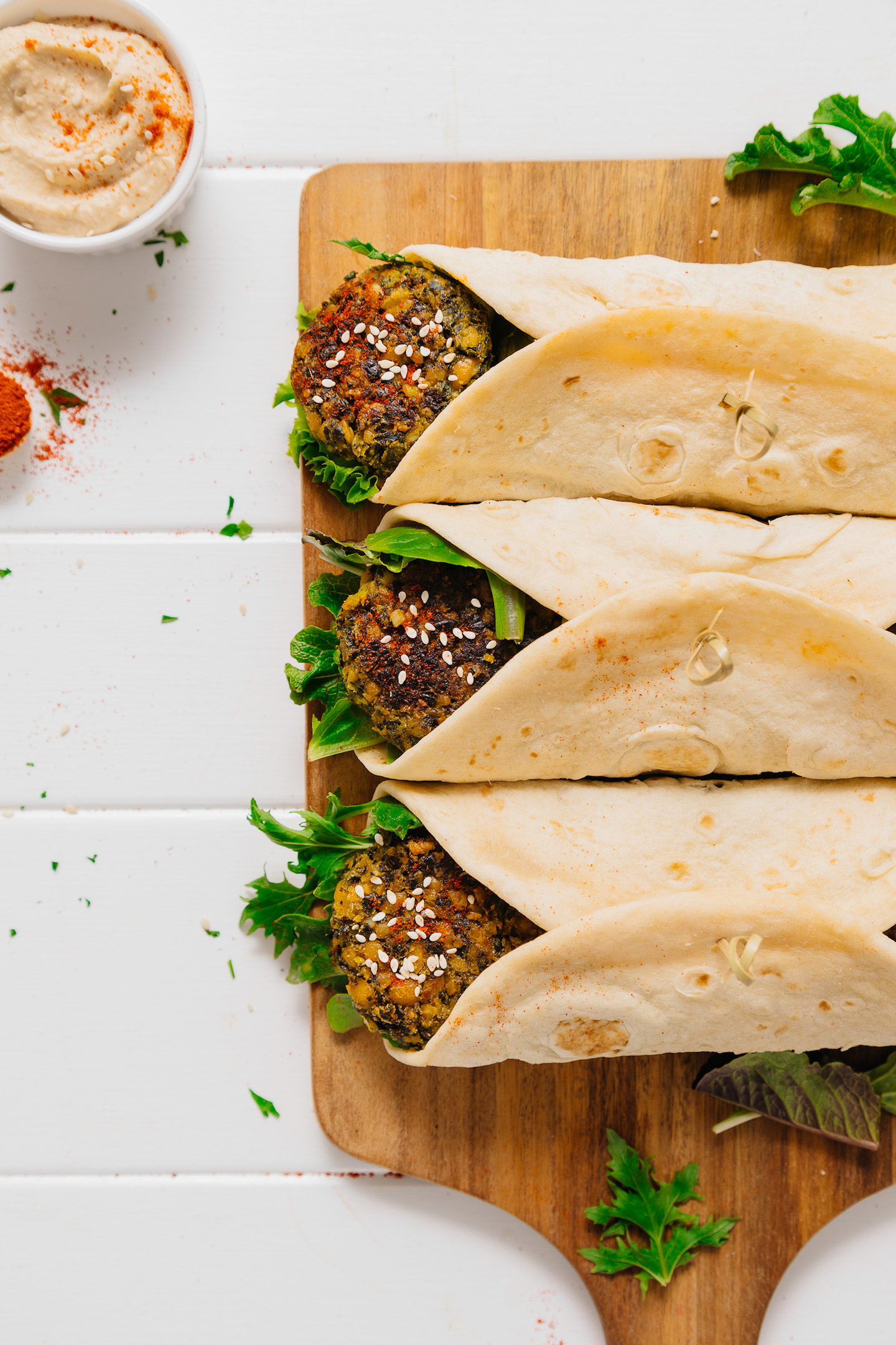 Wood cutting board with three Kale Falafel Hummus Wraps beside a bowl of hummus