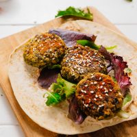 Making a healthy vegan Kale Falafel Hummus Wrap on a wood cutting board