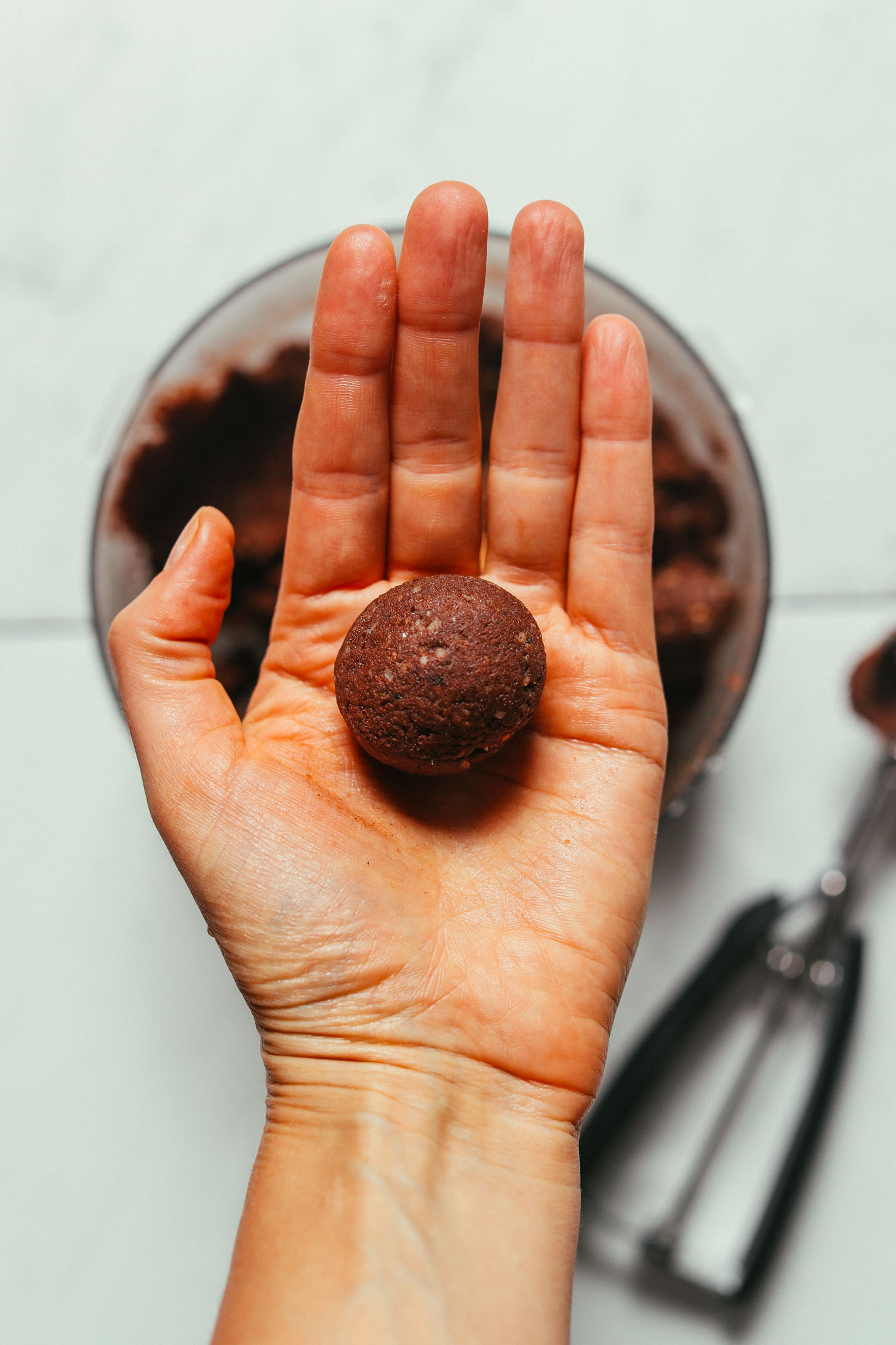 Holding up a Brownie Bliss Ball made with almond pulp and cacao powder