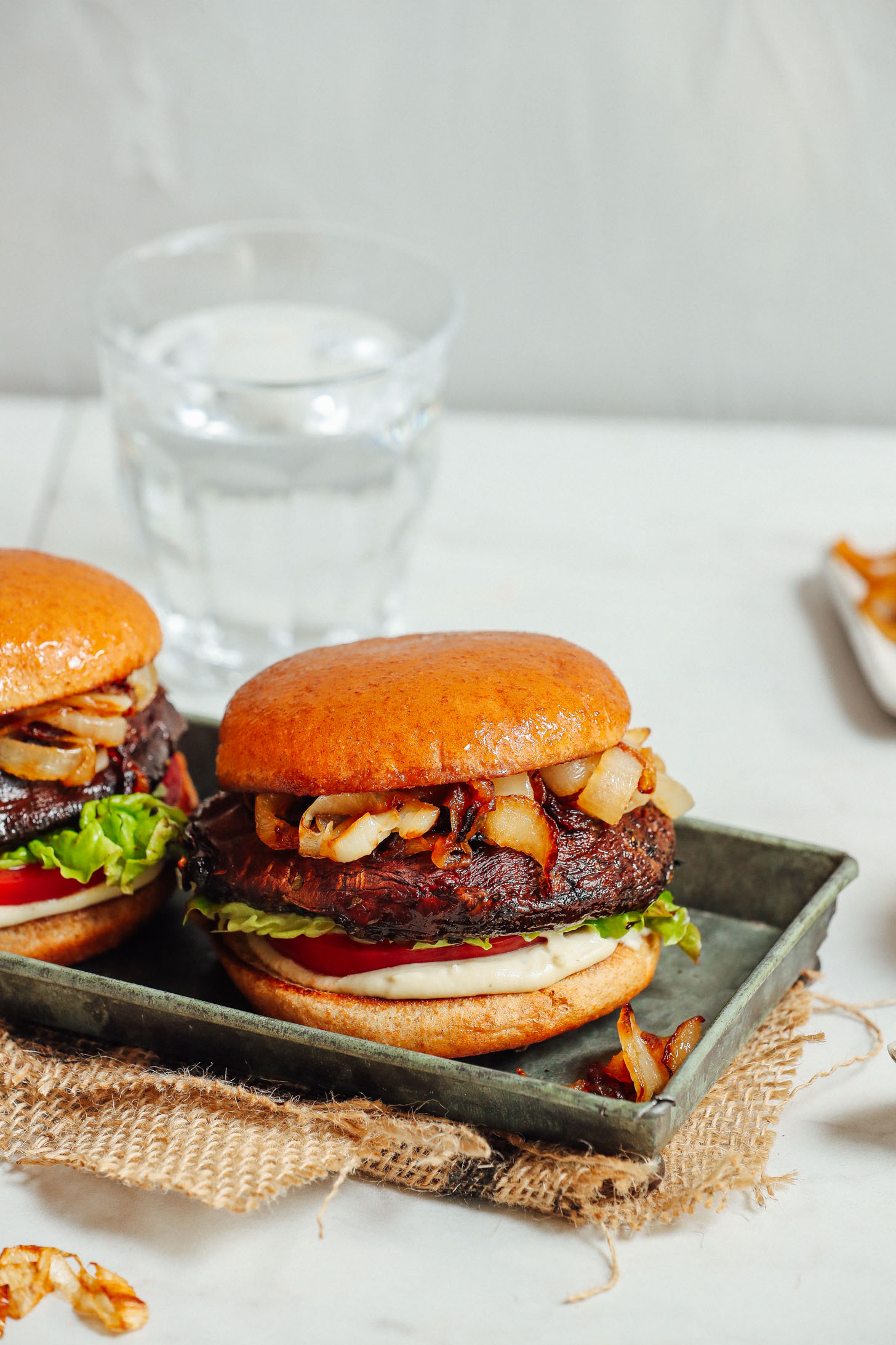 Glass of water and tray with two Balsamic Marinated Portobello Burgers with Caramelized Onions and Garlic Aioli